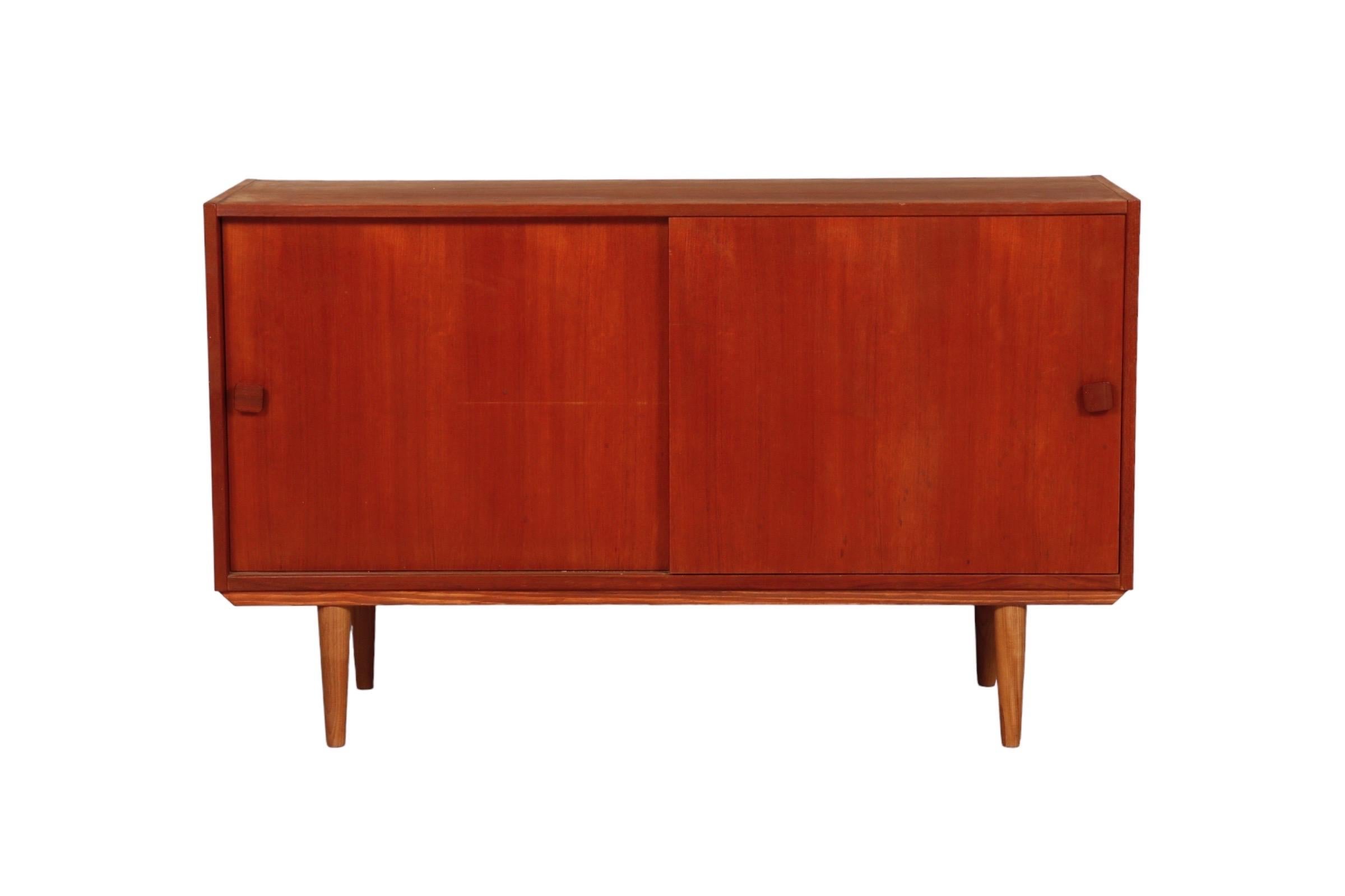 A Danish mid century low sideboard in teak. Two sliding cabinet doors reveal storage with a shelf on each side. Stands on round tapered legs.