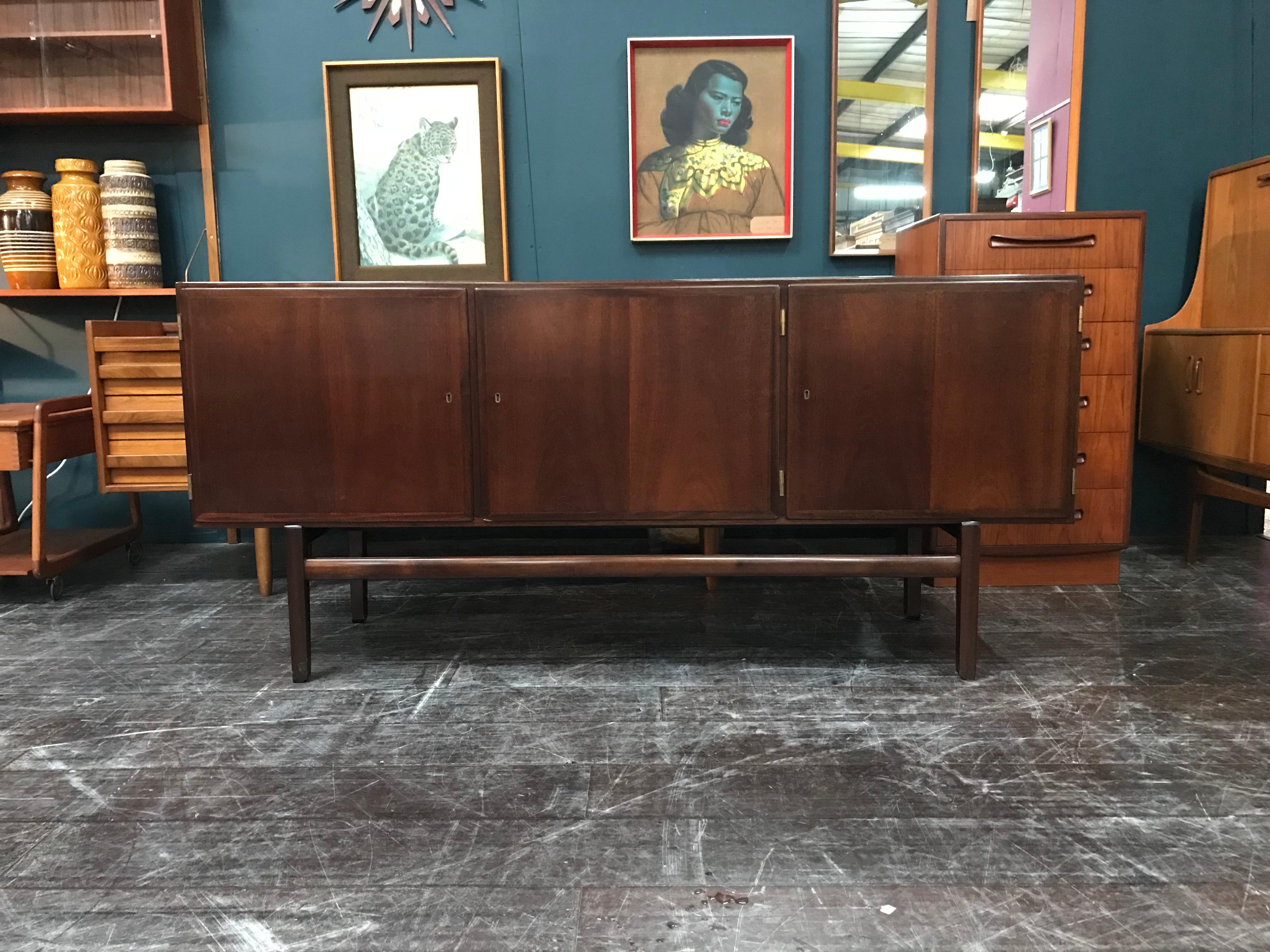 Ole Wanscher designed this clean-lined sideboard for Poul Jeppesen in the 1960s. Constructed of a rich stained mahogany, the raised case features three locking doors (with the original brass key) that conceal shelves on either side of two shallow