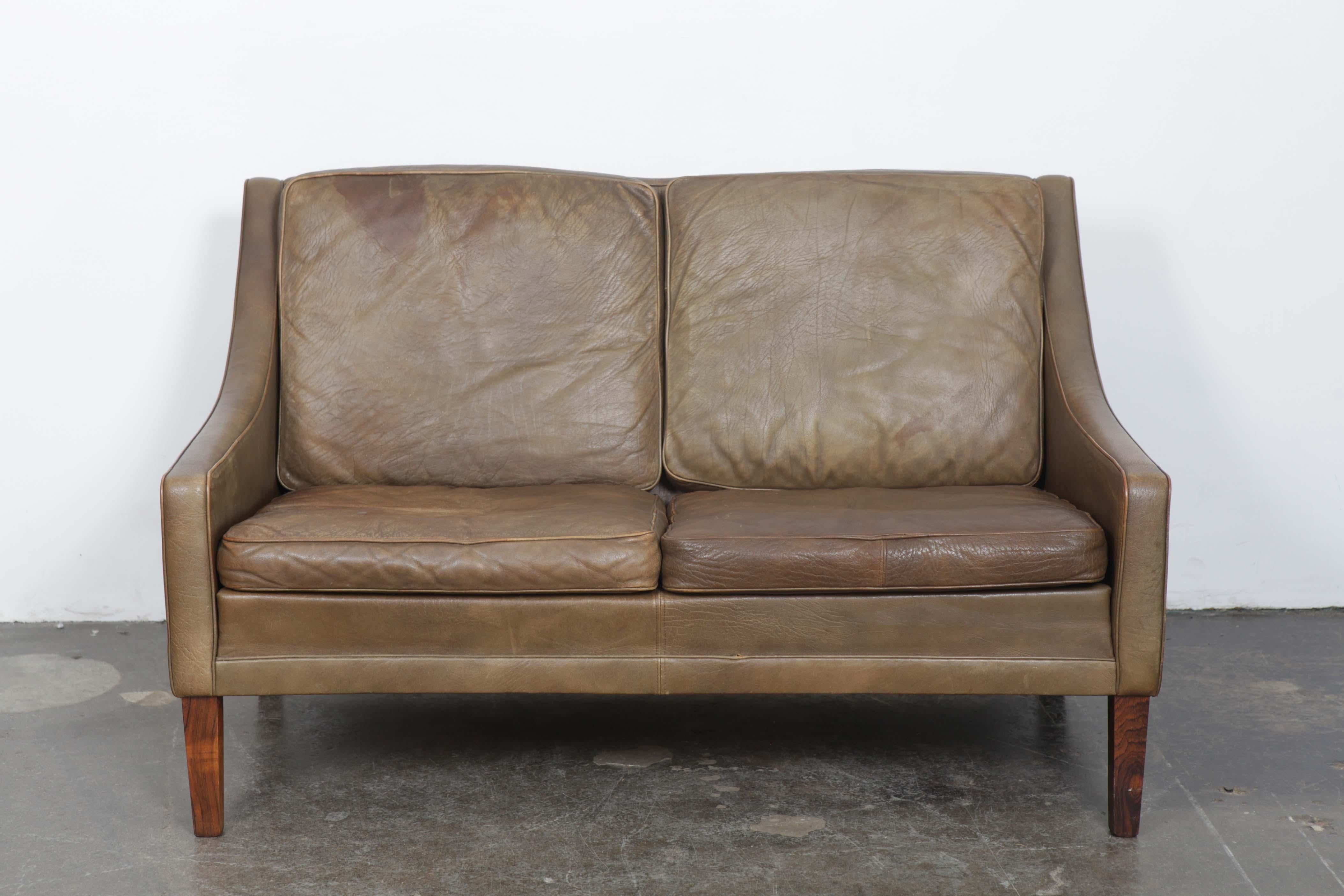 1960s 2-seat Danish Mid-Century Modern sofa in the manner of Børge Mogesen, in original leather with stained solid wood legs. The sofa has no tears or rips or other damage but does have discoloring and patina throughout.