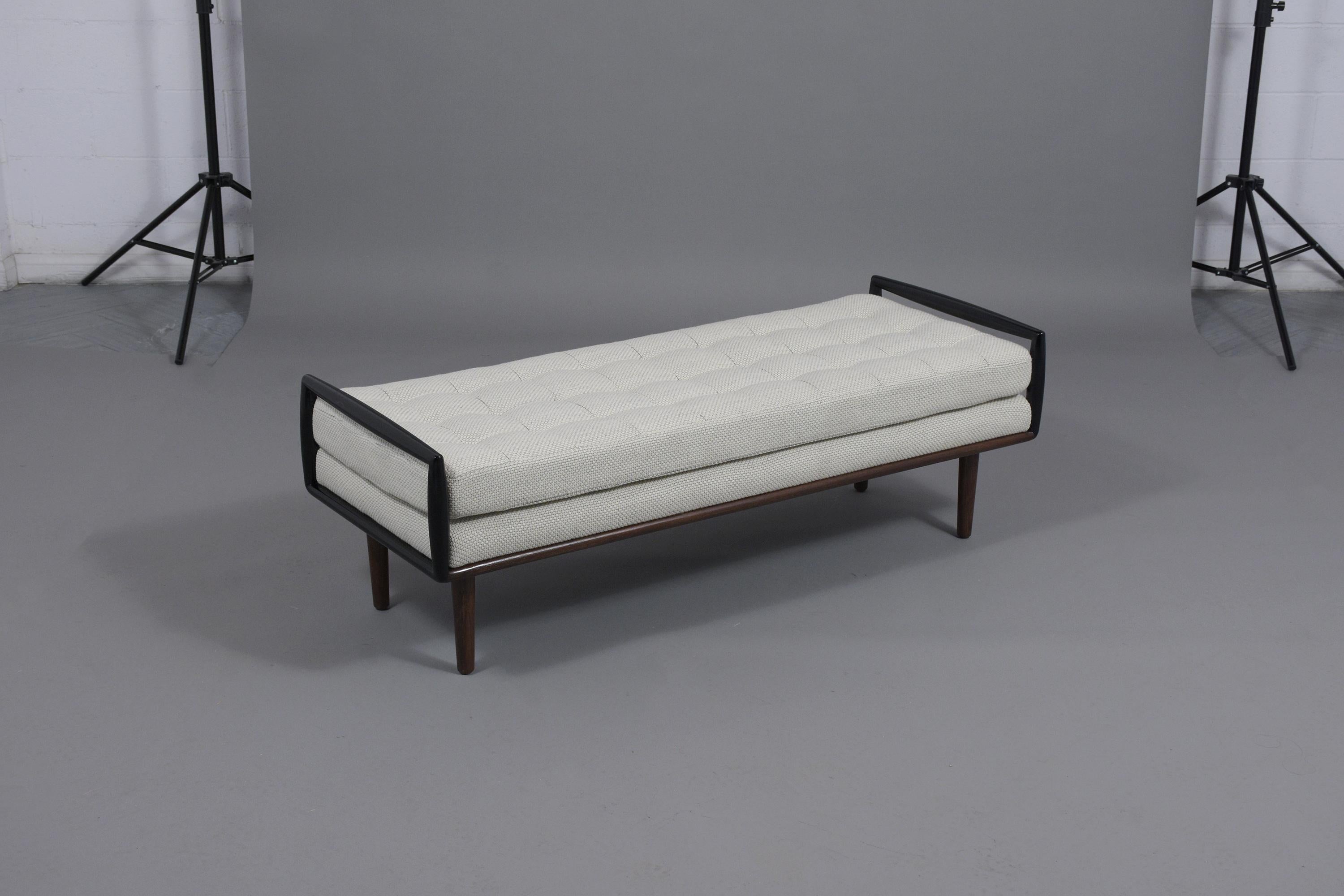 A slick Danish modern bench is hand-crafted out of rosewood and has been fully restored. The two-seater bench features a carved framed raise by four carved tapered legs newly finished in dark mahogany and ebonized color combination with a lacquer