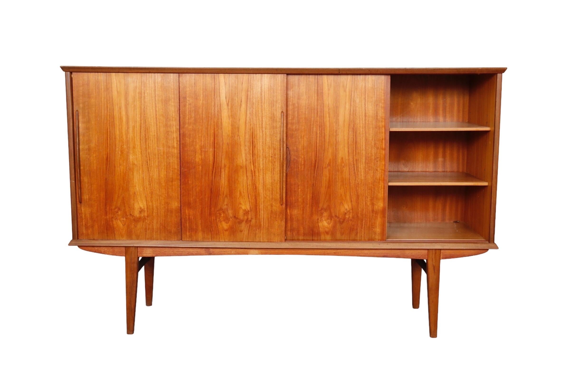 A Danish mid century modern teak buffet. Sliding cabinet doors reveal a mirrored bar area on the left above four dovetailed drawers that open with recessed handles. Drawer fronts are decorated with matching veneers. Storage compartments to the right