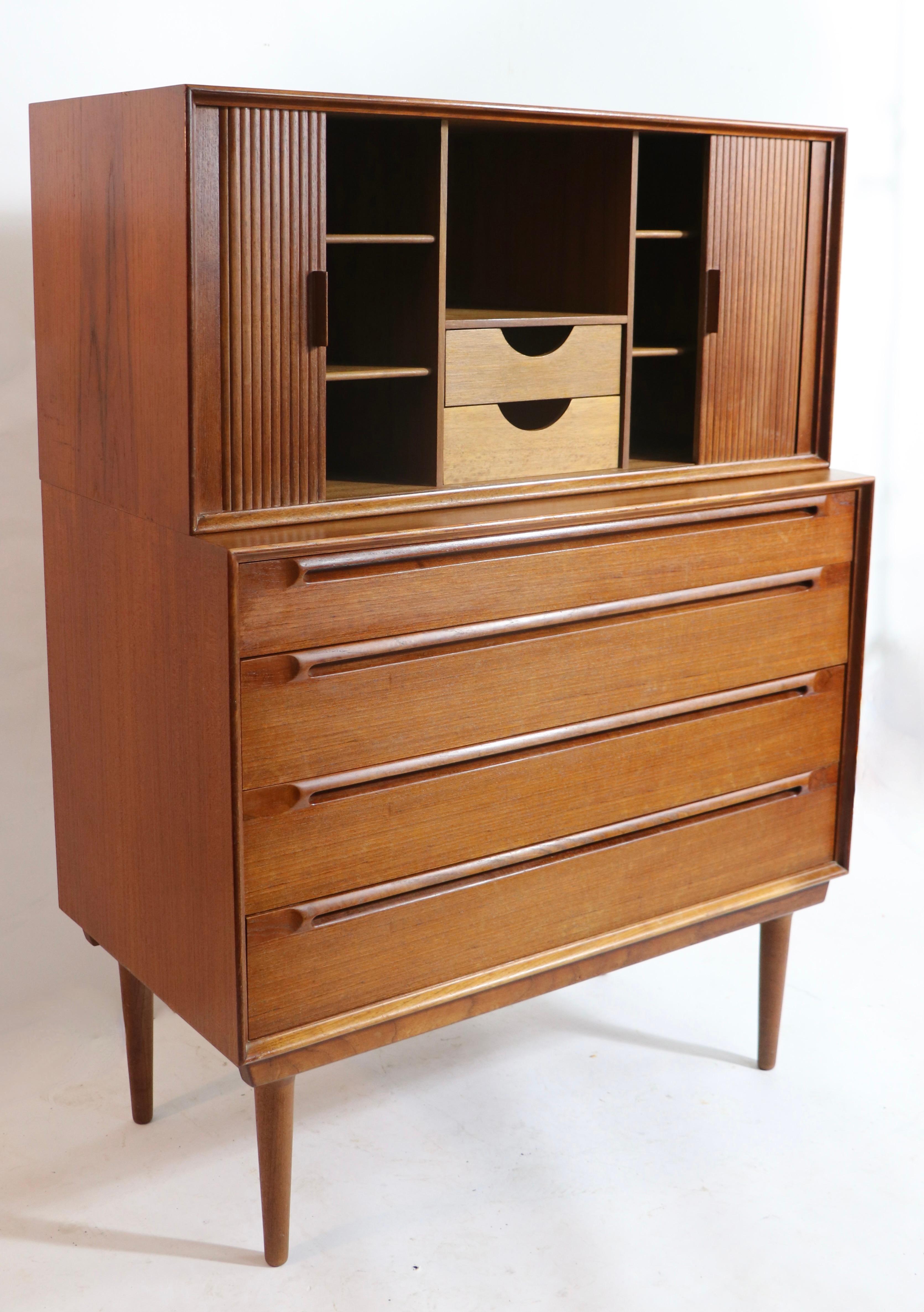 Interesting two-part chest on chest, designed by Sven Ellekaer. The chest features two separate cabinets, including the top piece ( 37.5 W x 17.5 H x 16.5 H in. ) which has a tambour roll front that opens to selves and interior drawers, over a four