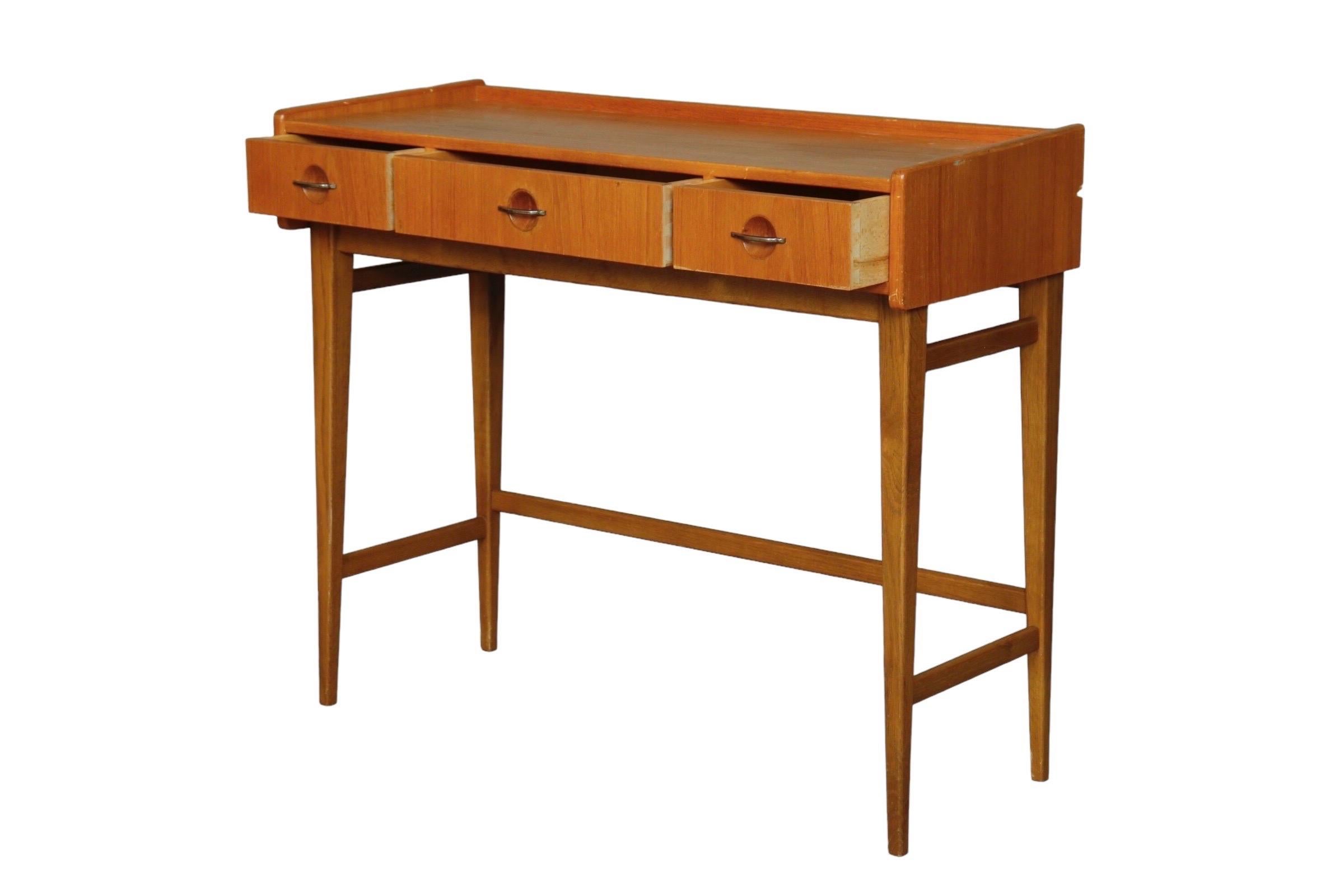 A Danish Mid-Century Modern console table made of teak. Three dovetail drawers open with curved metal bar handles. Square tapered legs are supported with an open box stretcher.

Measures: Length about 34.5”. Width about 13.75”. Height about 29.25”.