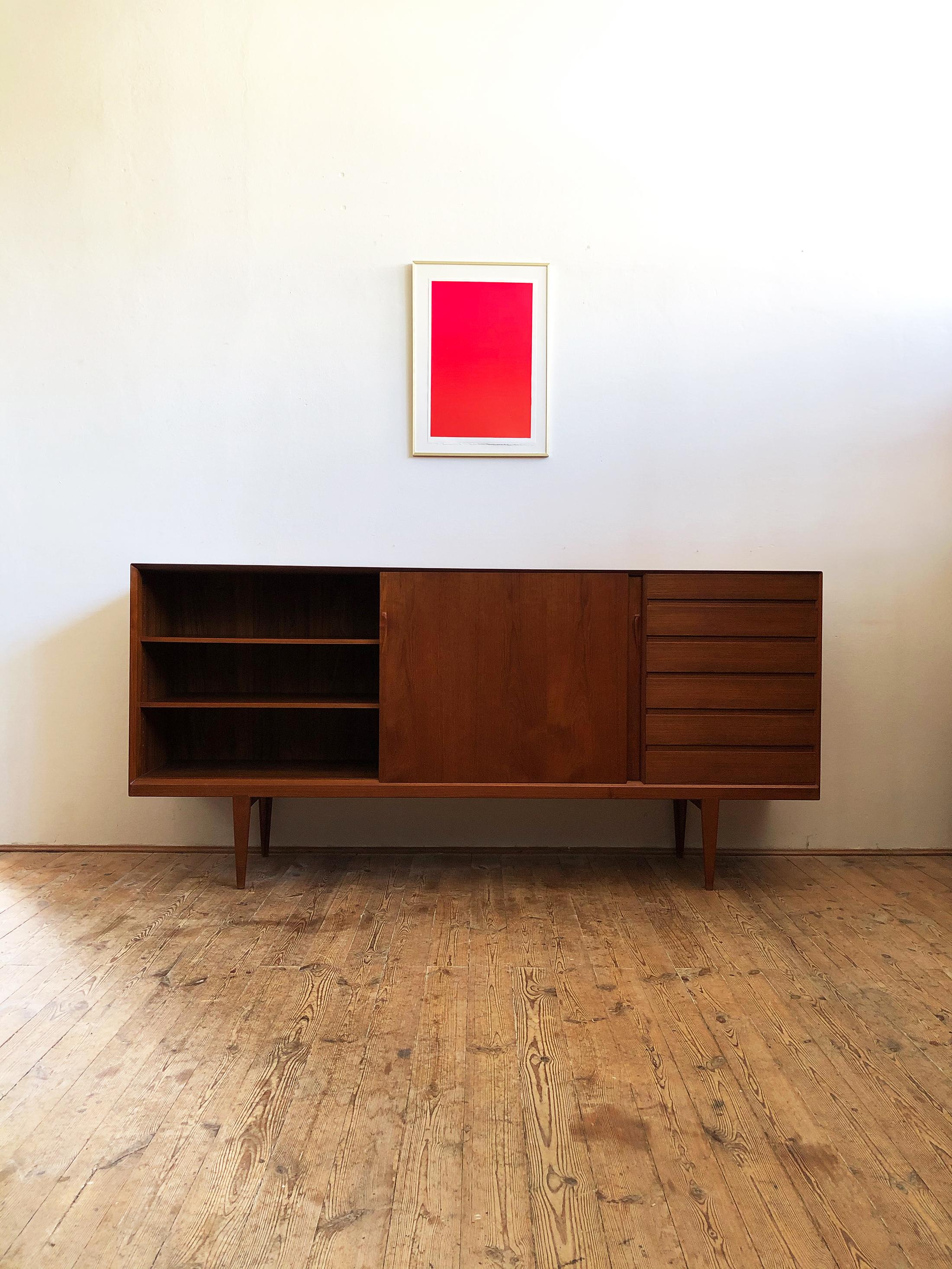 This Mid-Century Modern teak sideboard was designed in the 1950s by Henry Rosengren Hansen for Brand Møbelindustri. It shows exquisite Danish craftsmanship and offers plenty of storage space on four tapered legs and lots of beautiful