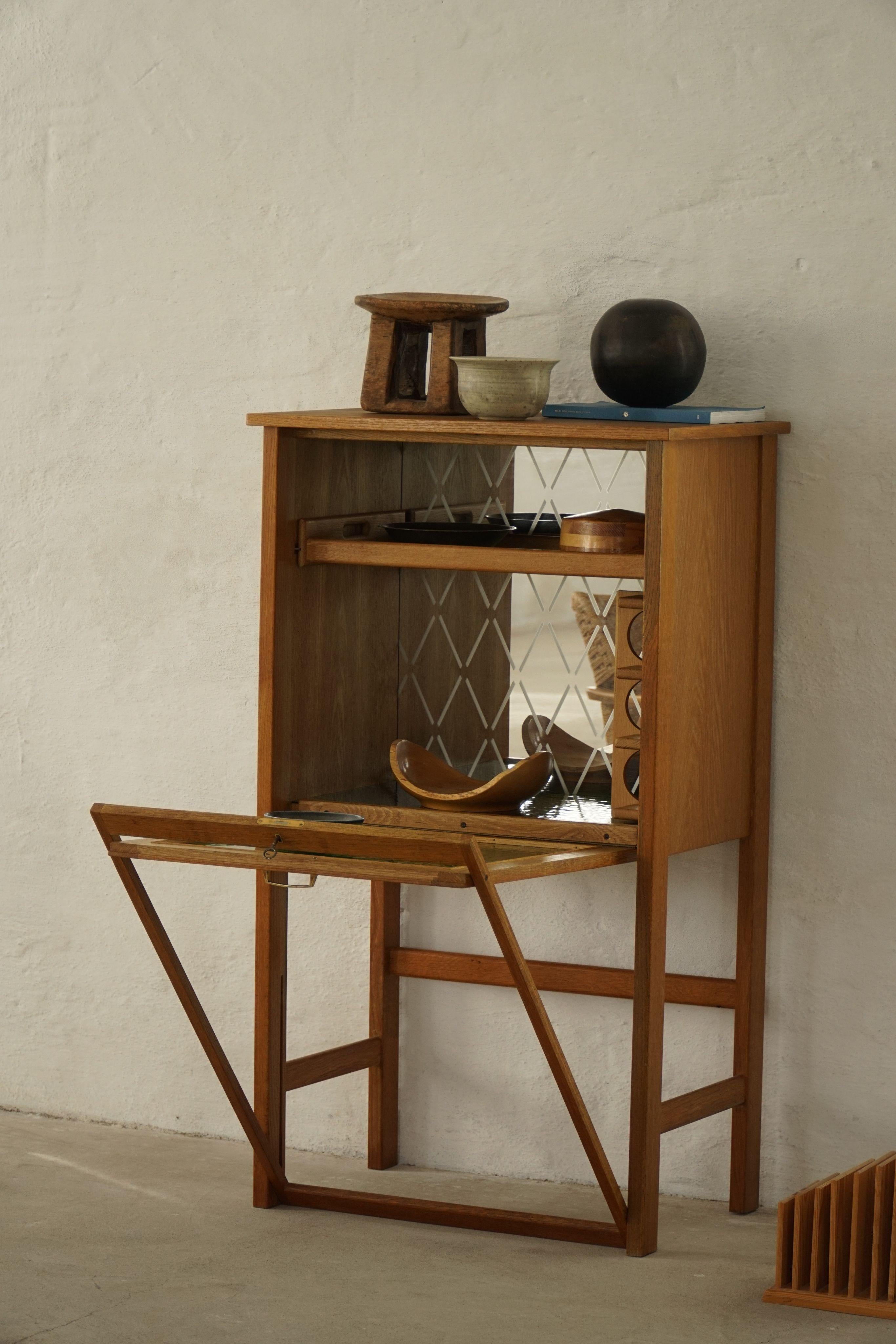 A refined bar cabinet from the 1960s, crafted in warm-toned oak and fronted with geometric green glass panels. The textured glass catches light beautifully, forming subtle square patterns that shift with the room’s atmosphere.

Inside, a mirrored