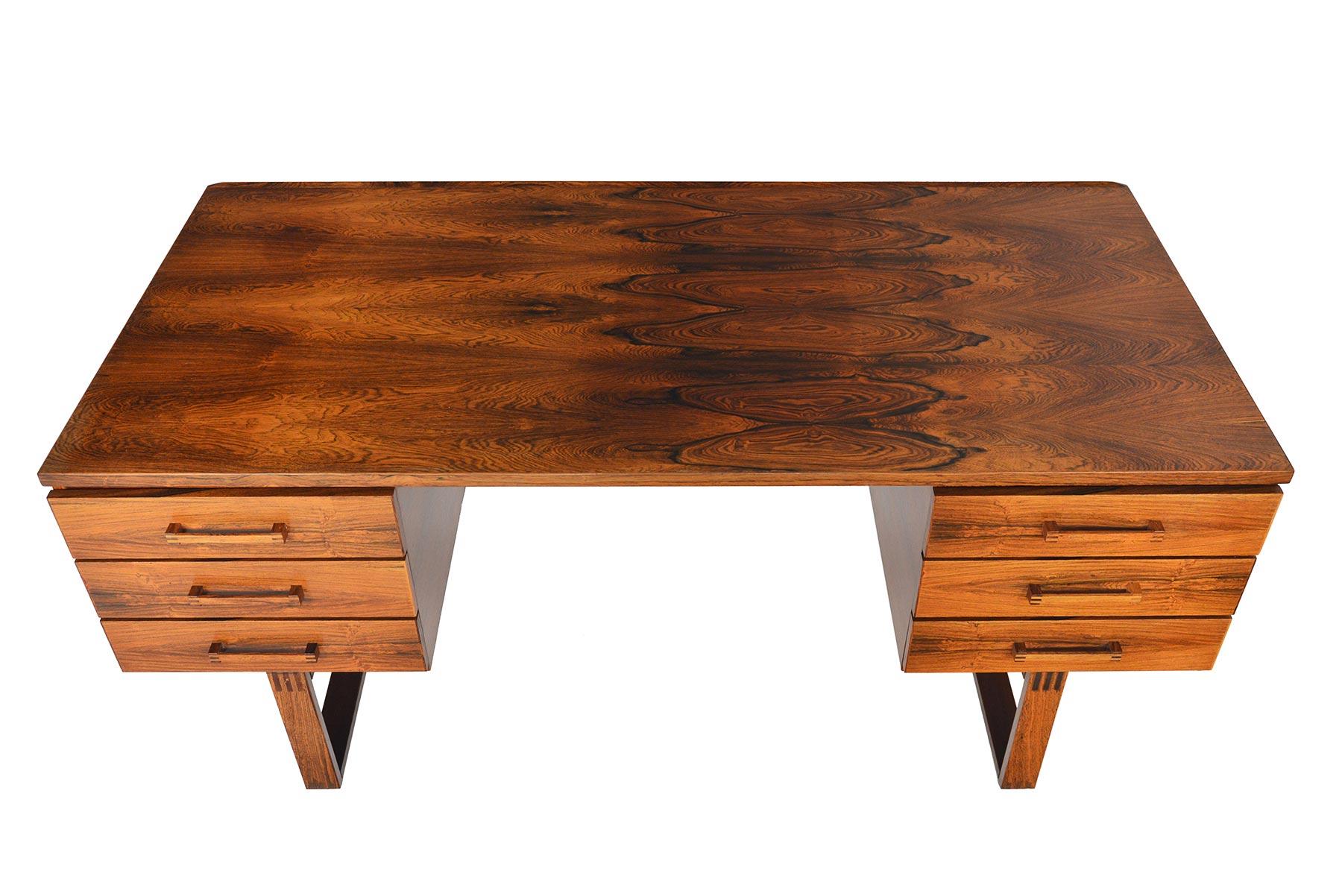 This Danish modern executive desk in Brazilian rosewood was designed by Henning Jensen and Torben Valeur for Dyrlund in the 1960s. The spacious kneehole is nestled between two banks of drawers. Each drawer features a solid rosewood, finger- joined