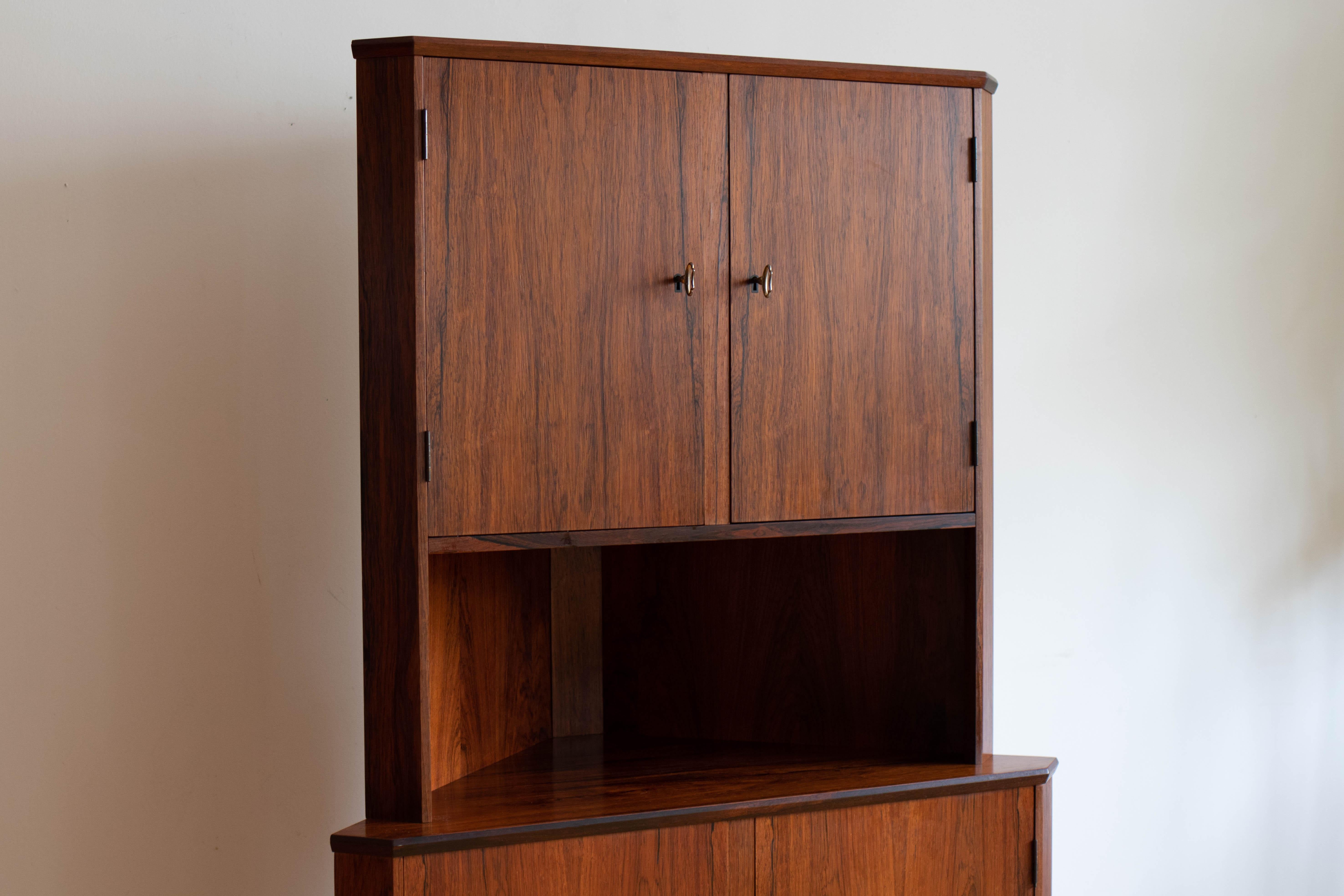 Scandinavian Mid-Century Modern rosewood corner cabinet.
Just imported from Copenhagen, Denmark.
Two double locking cabinet doors.
Includes two vintage brass keys.
Adjustable triangle shelving, not usually seen in corner units. 
Excellent vintage