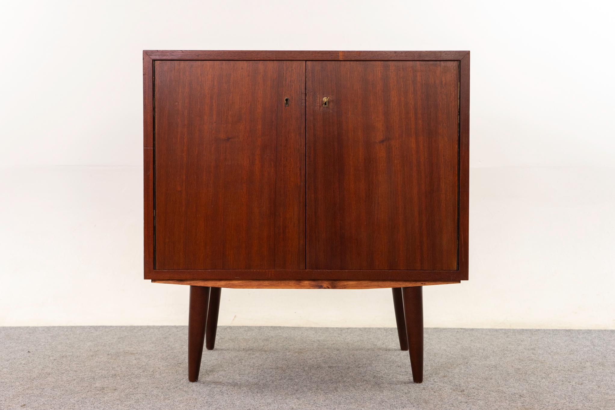 Armadio danese in mogano, anni '60 circa. Il design pulito e semplice delle linee mette in risalto l'eccezionale impiallacciatura abbinata ai libri. Porte con chiusura a chiave, ripiano regolabile (non originale) e gambe eleganti e sbarazzine.