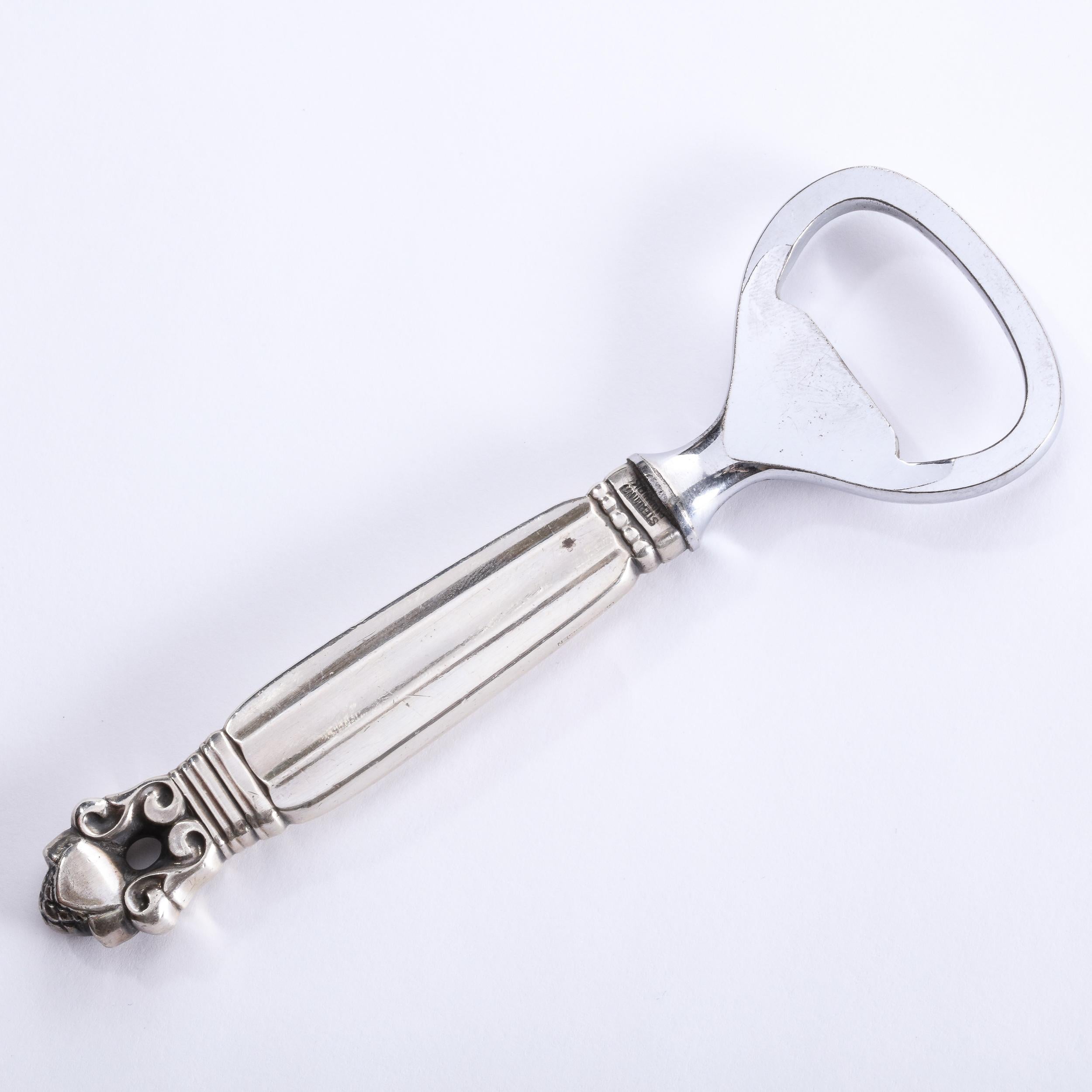 This elegant Mid-Century Modern bottle opener was realized in Denmark, circa 1960. It features a neoclassical stylized scroll form base; a reeded body; as well as channel detailing at its base and neck- in lustrous sterling silver. This is a