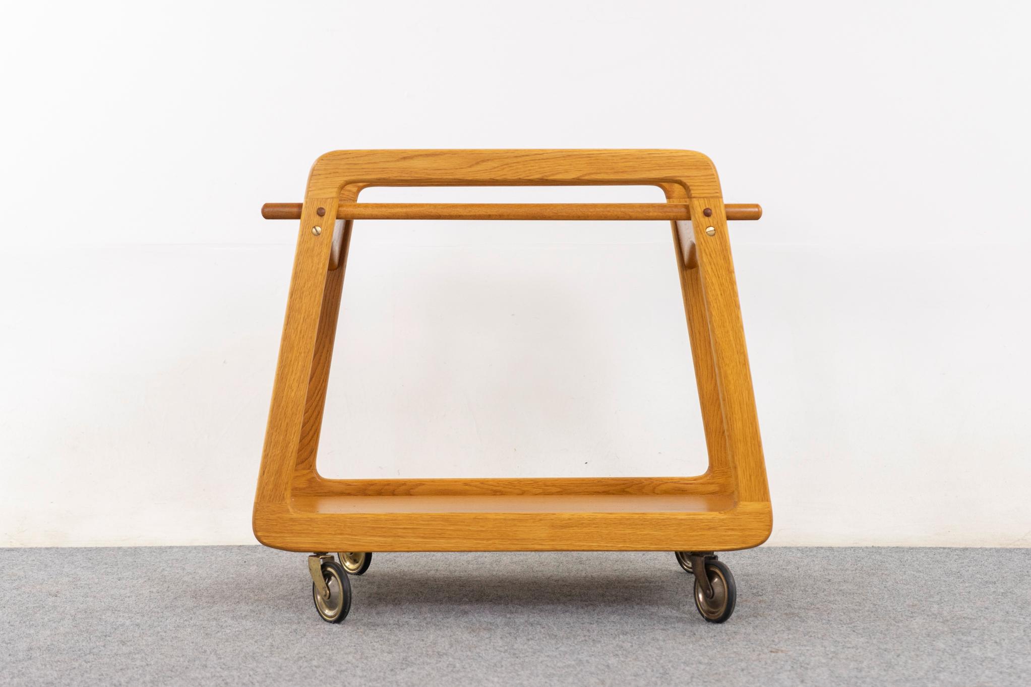 Oak Danish bar cart, circa 1960s. Perfectly petite with a striking silhouette. Charming reversible flip top doubled as a serving tray! Grey melamine top is perfect for serving drinks—original smooth operating casters.  

Please inquire for
