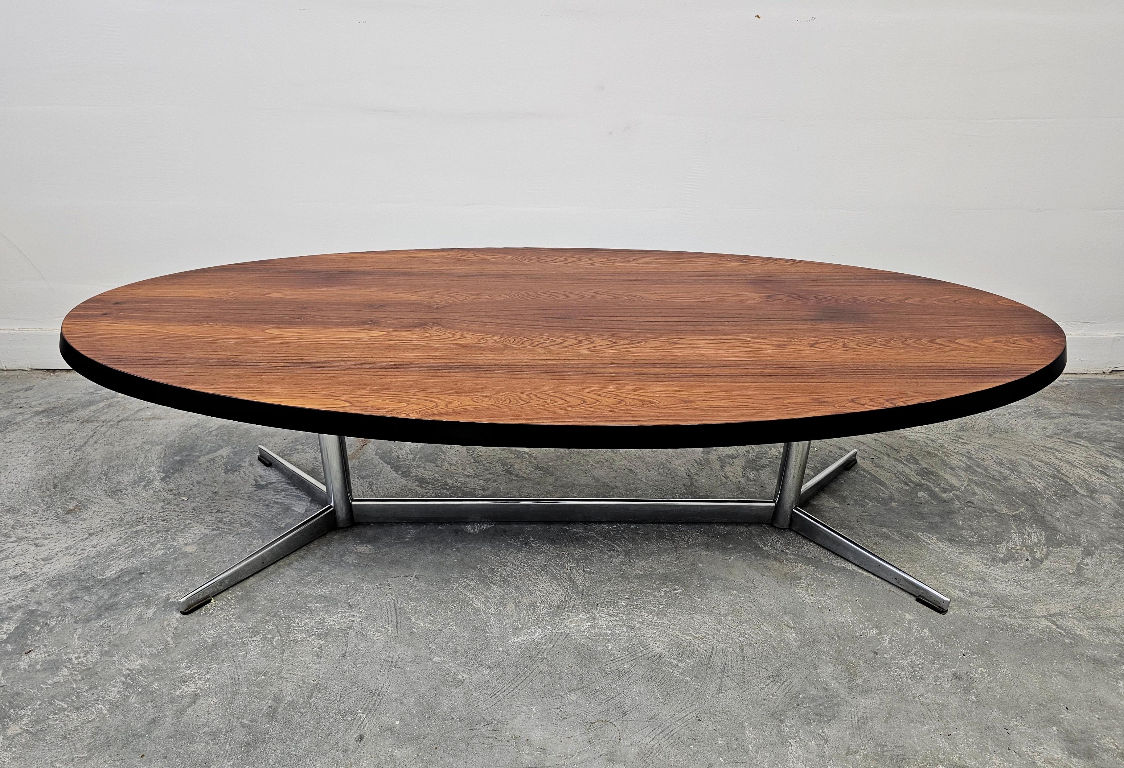 Dans cette annonce, vous trouverez une magnifique table basse ovale et élégante de style moderne du milieu du siècle dernier. Le plateau de la table est réalisé en placage avec de belles veines de bois, fixé sur des pieds en acier. Fabriqué au