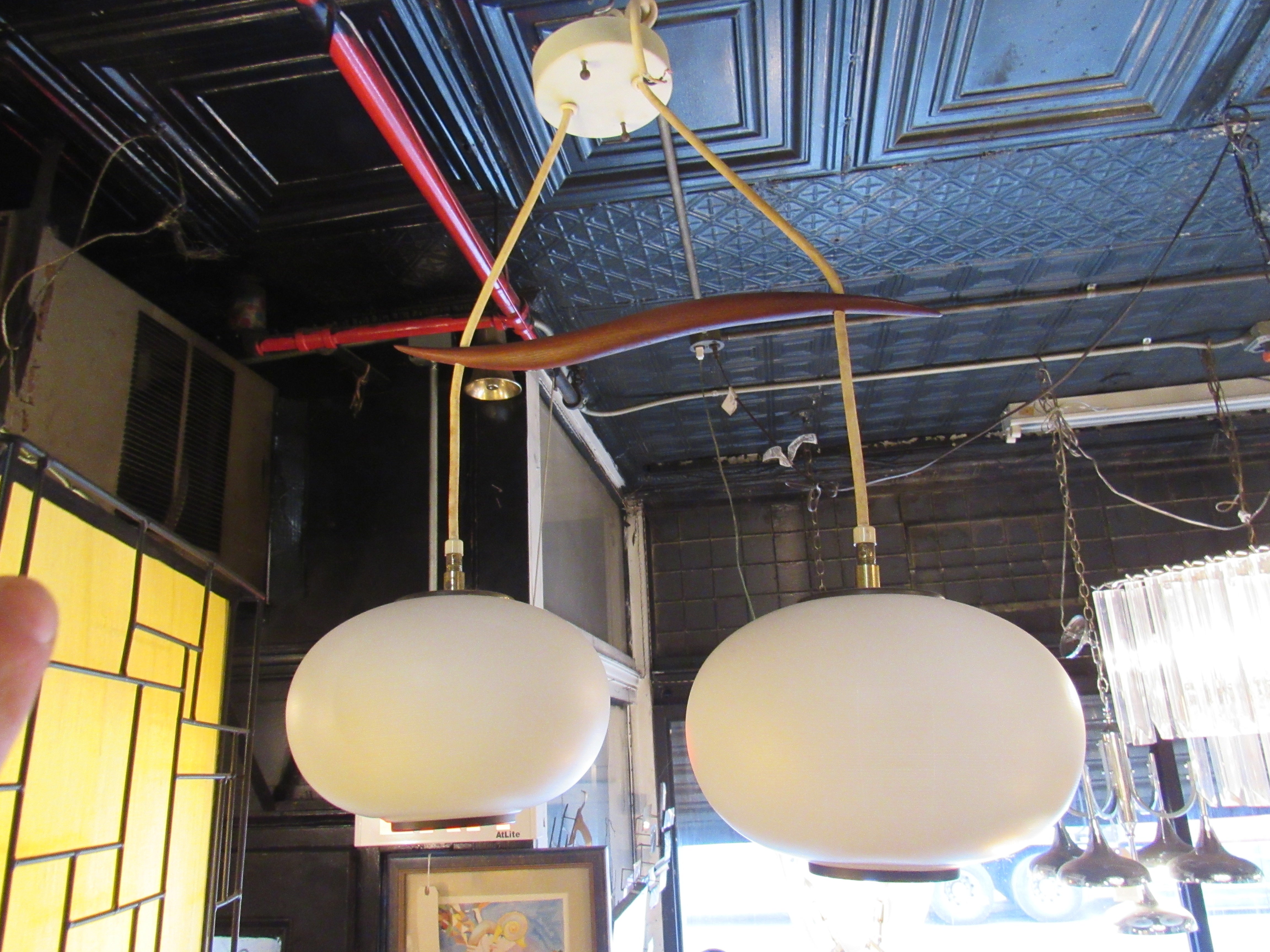 Avec deux grands globes et une bande de bois qui les relie, cette suspension vintage est un joyau de la modernité du milieu du siècle. Une lumière douce émane des abat-jours en verre laiteux, suspendus à un cadre en teck sculpté.
Veuillez confirmer