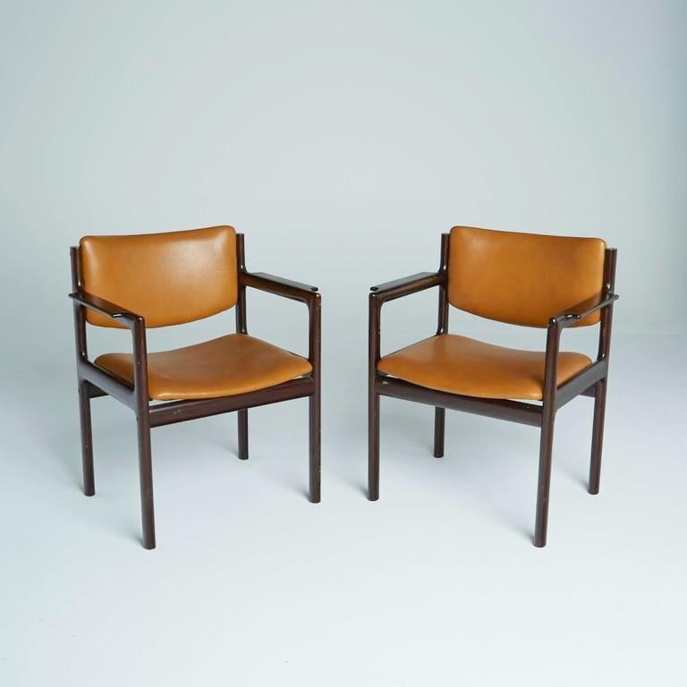 This pair of caramel Mid-Century Modern armchairs are as durable in construction as they are attractive in their Danish modern design. The caramel leatherette upholstery of the seats and backs of each chair is framed by rich, dark rosewood with