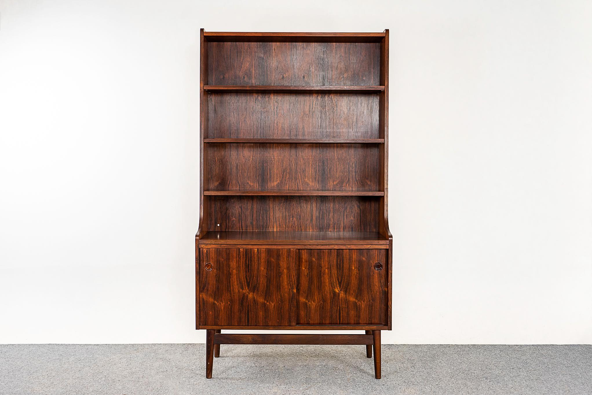 Rosewood Danish bookcase by Johannes Sorth, circa 1960's. Stunning grain patterns and beautiful tapering silhouette. Open bookshelf with 3 adjustable shelves, sliding doors reveal a shelf within. Solid wood legs with a beautiful floating effect.