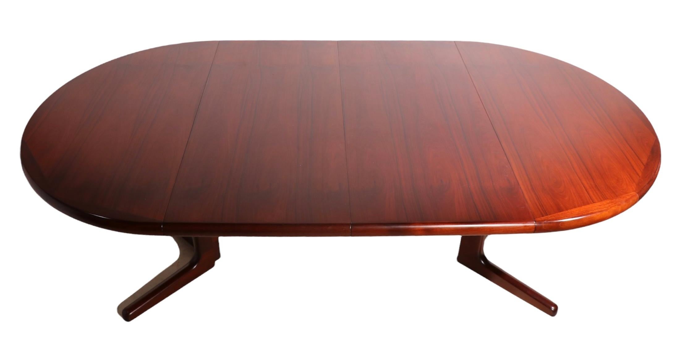 Impressive Danish Modern dining table in rosewood, including 2 original leaves ( 19.75 in. W each. ). The table rests on an architectural split pedestal base, it is circular when closed, 47 in. Dia. and becomes an oval when the leaves are in place,