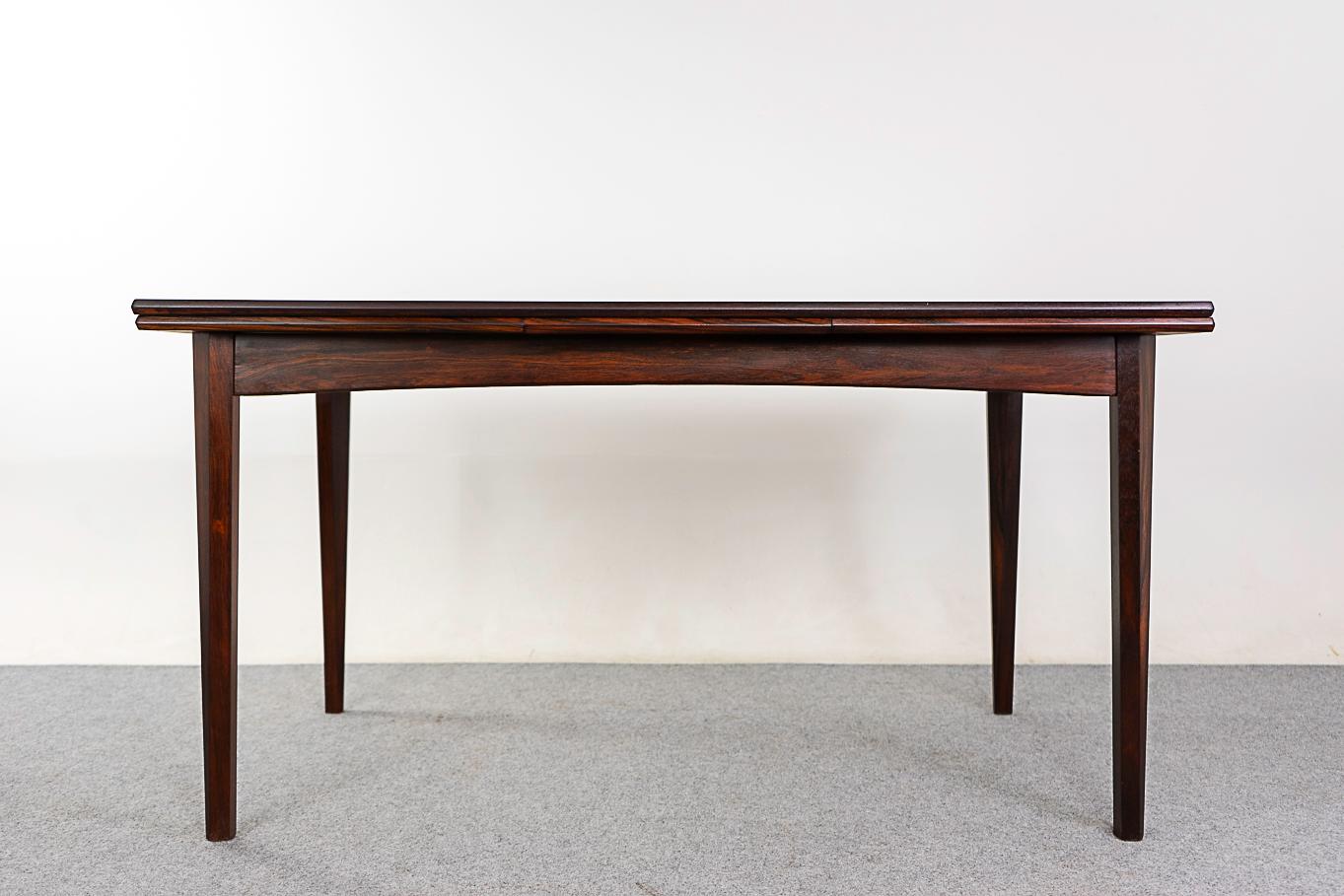 Rosewood Danish dining table, circa 1960's. Top is framed in solid wood, center panels feature highly figured veneer with book-matched grain. Sultry sculptural legs and arched apron. Self-storing leaves slide out from each end to extend the table