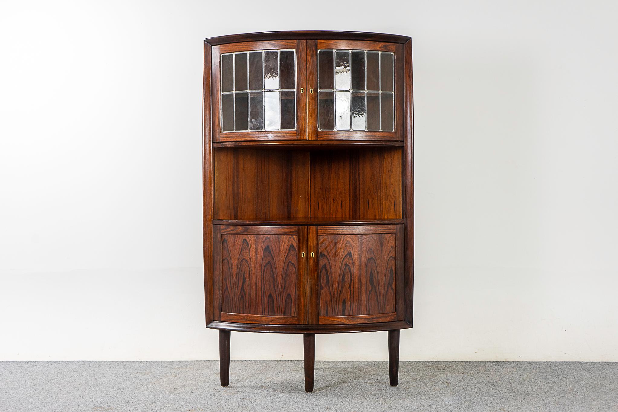 Rosewood & glass Danish modern corner cabinet, circa 1960s. Unique locking cabinet with round profile and figurative veneer throughout. Hide away clutter, show off your fancy vintage cocktail glasses and barware! Make mine a double - we have a pair