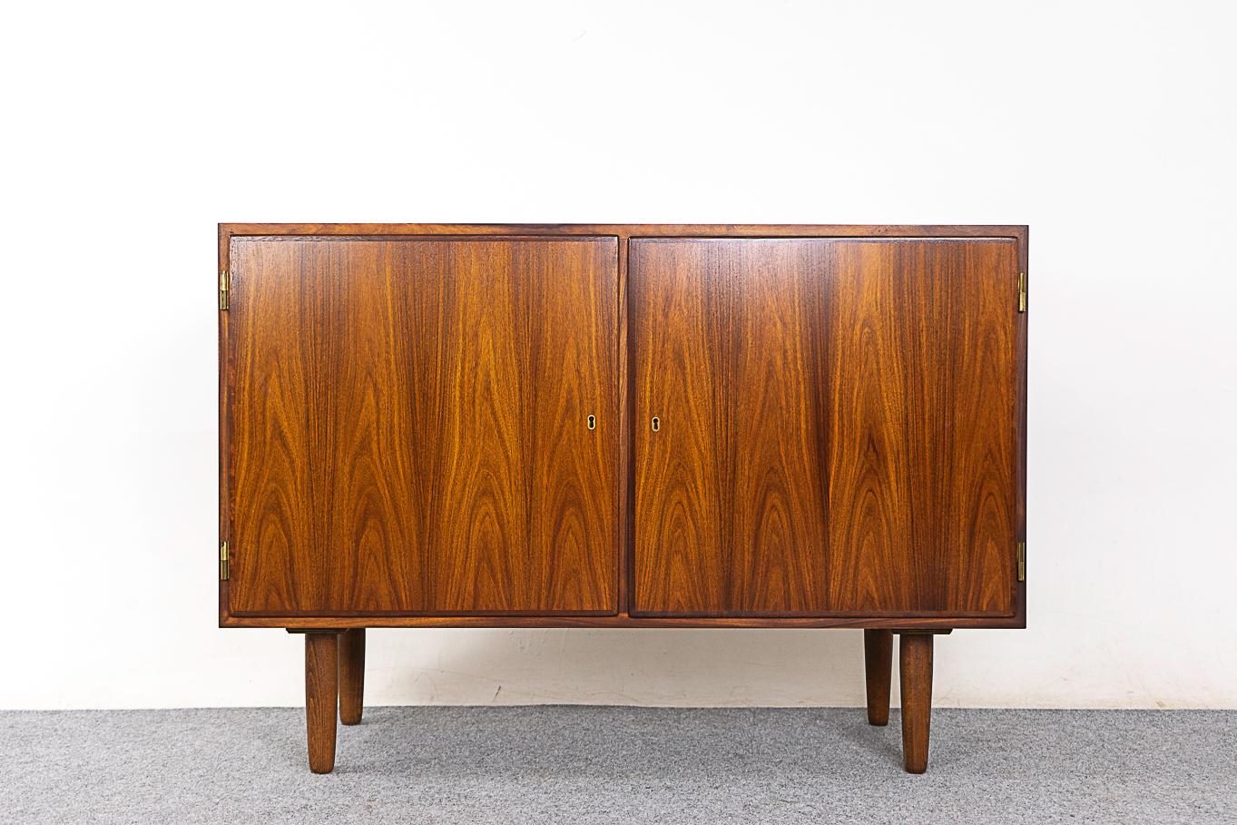 Rosewood mid-century cabinet by Hundevad, circa 1960's. Clean, simple lined design with exceptional book-matched veneer. Locking double doors, 2 adjustable shelves, 3 sleek drawers and tapered legs. Compact size!