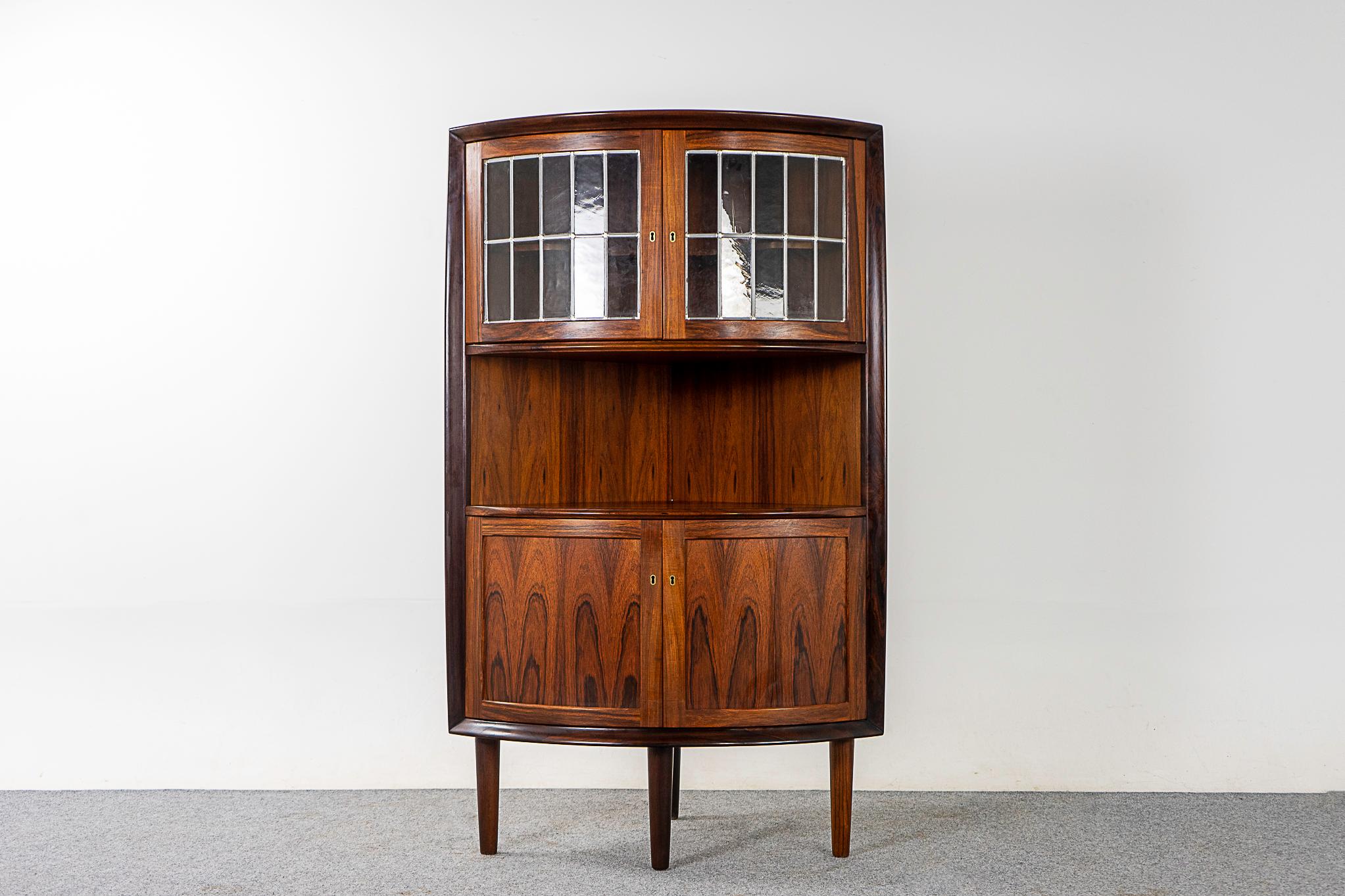 Rosewood & glass Danish modern corner cabinet, circa 1960s. Unique locking cabinet with round profile and figurative veneer throughout. Hide away clutter, show off your fancy vintage cocktail glasses and barware! Make mine a double - we have a pair