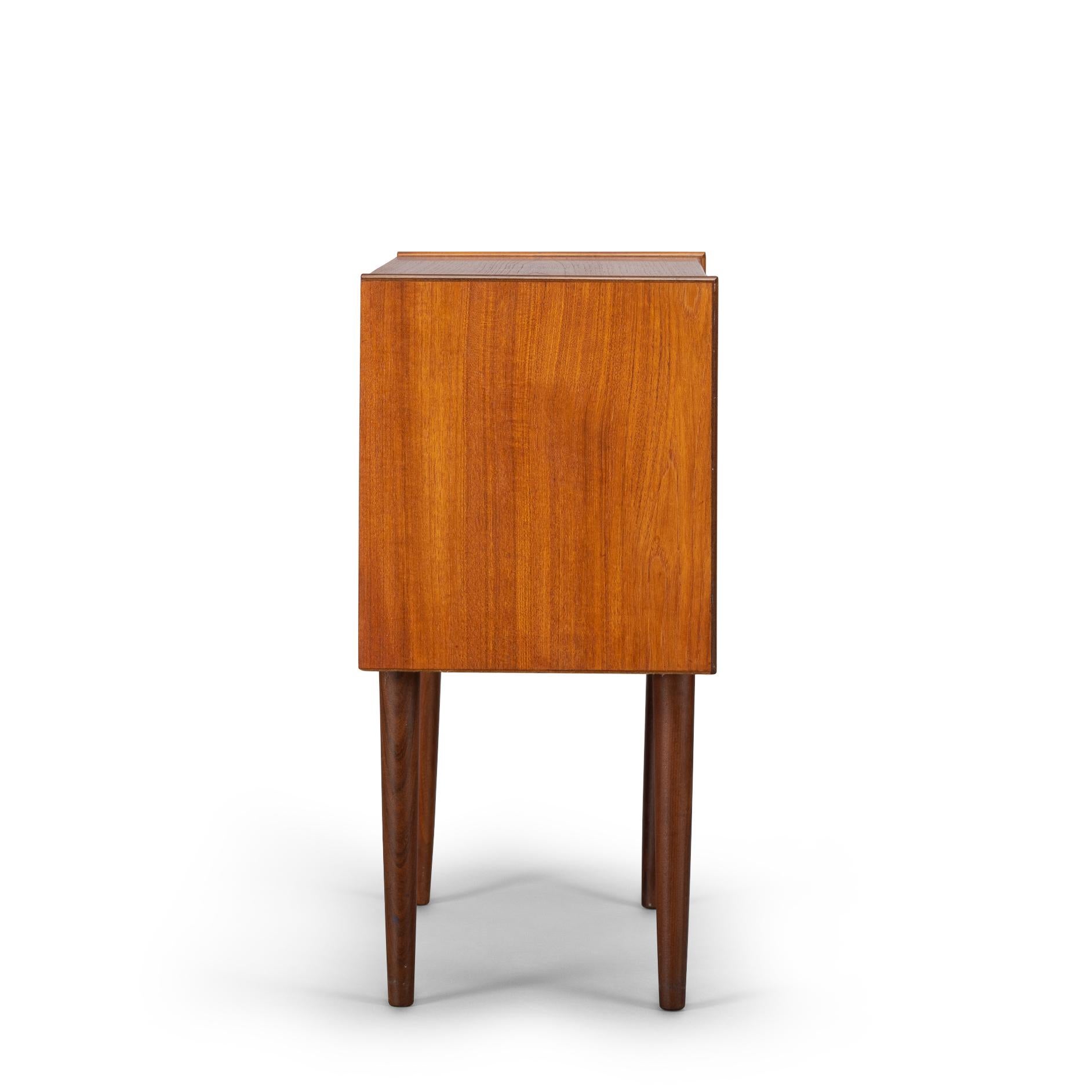 This petite Danish nightstand is made out of teak veneer in the late 1960s and embraces the period in full swing. Three drawers with fantastic rounded grips complete the sign of the times. The sides on top of this small chest are slightly raised.