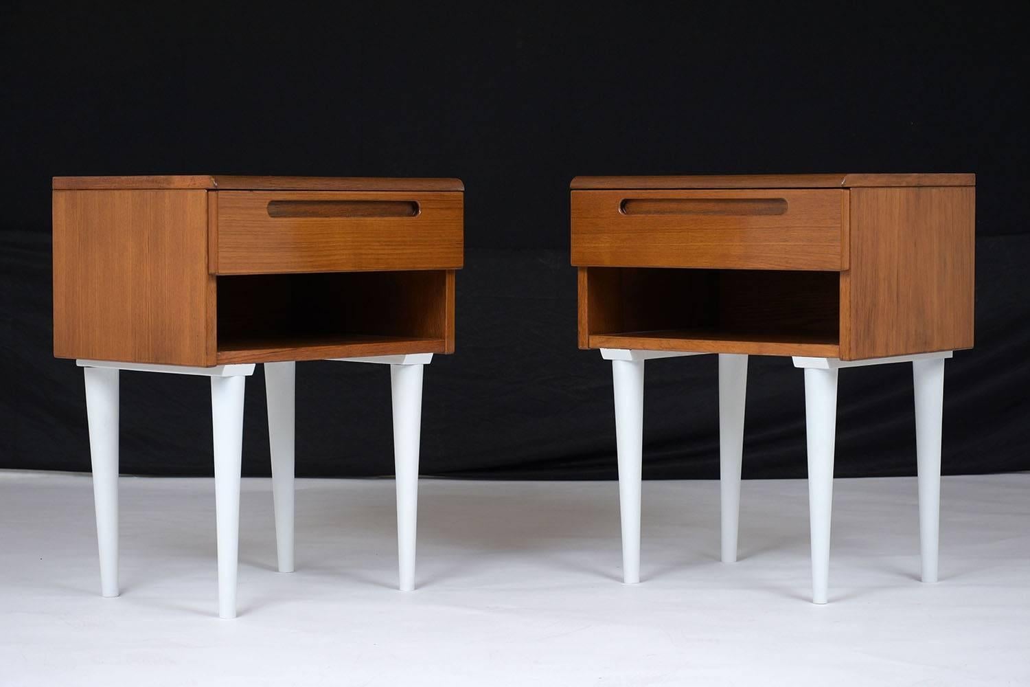 This pair of 1970s Danish Mid-Century Modern-style teak wood nightstands feature a walnut and white color combination with a lacquered finish. The body of the nightstands have a single drawer with handles carved into the drawer front and an open