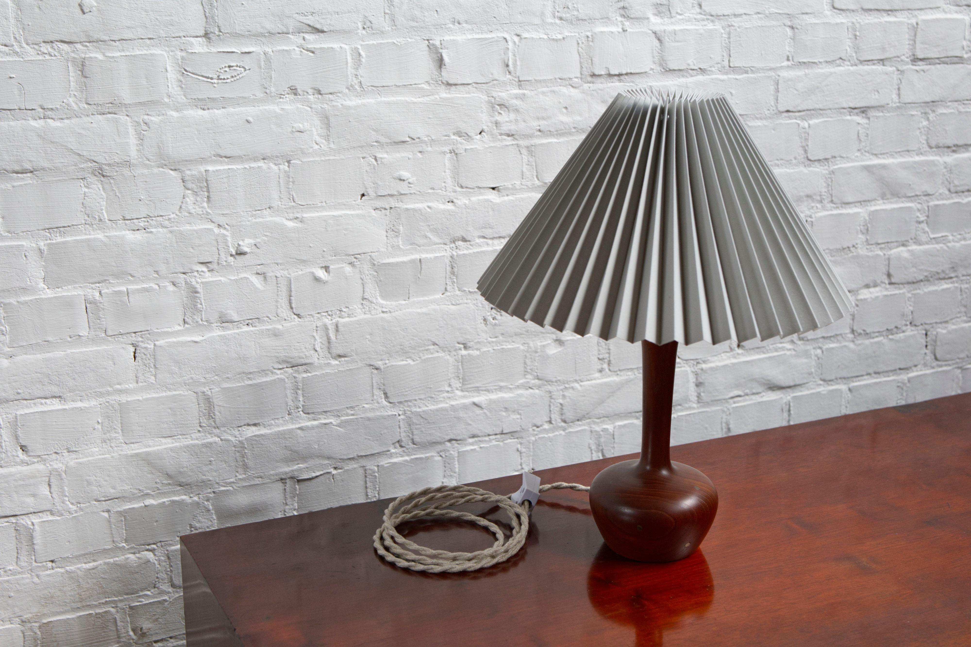 Danish Mid-Century Modern Teak Table Lamp with Inlayed Brass details an 
a off-white Linen pleated Lampshade – 1960s

A beautiful example of Danish mid-century craftsmanship, this 1960s table lamp features a turned teak base with elegantly inlayed