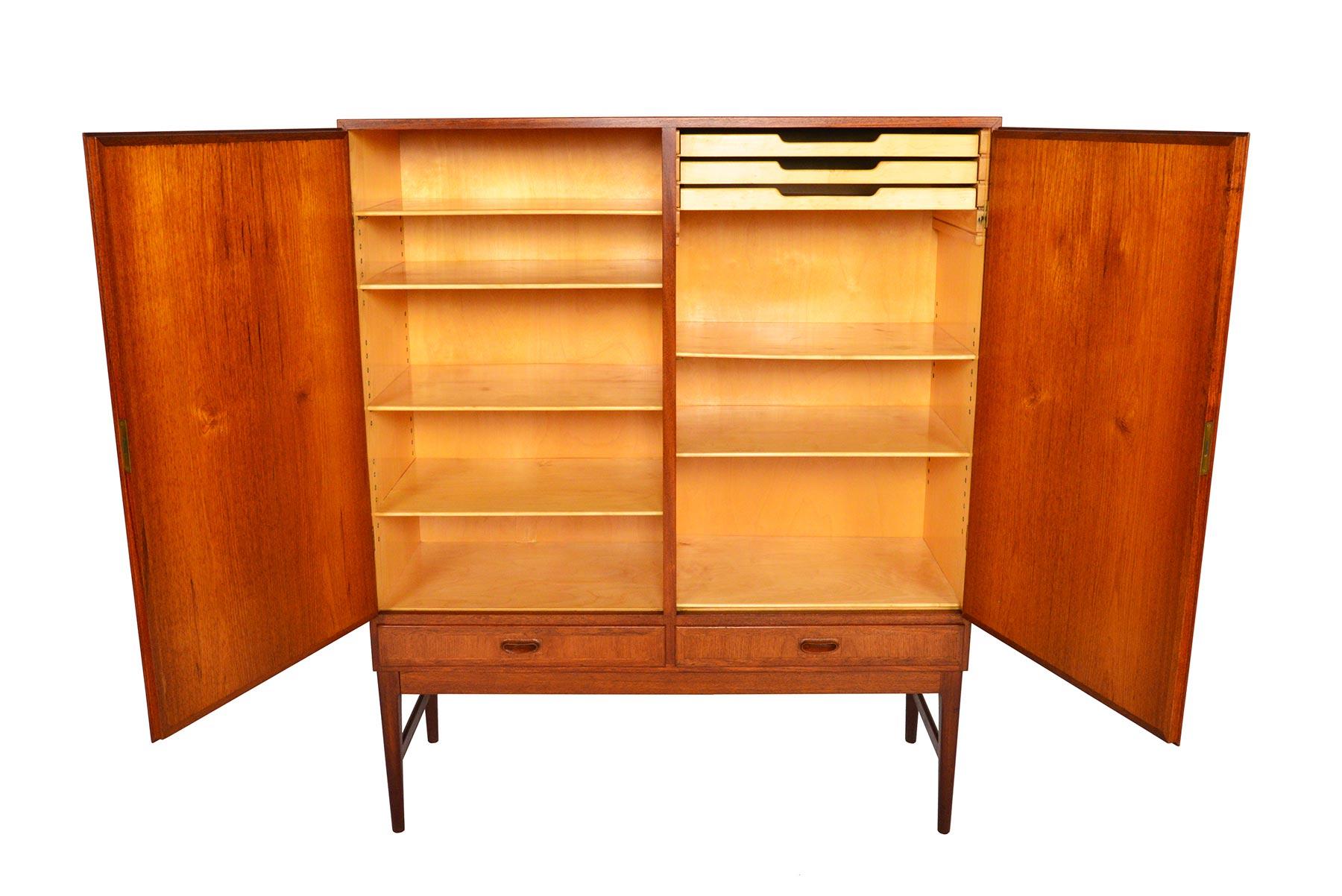 This Danish modern teak bureau offers a large storage capacity and sleek design. Two large locking doors open to reveal a beech- lined, two bay interior outfitted with six adjustable shelves and three felt lined drawers. Two lower drawers provide