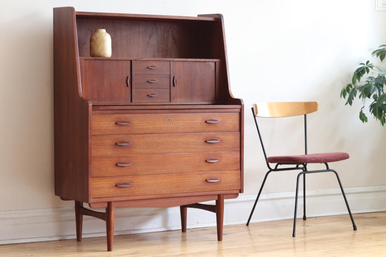Tall midcentury Danish modern teakwood secretary desk.
Just imported from Denmark!
Features tambour doors.
Divided mail organizer on the right; cubby space on the left with an old ink stain.
Hidden shelf extends to create a desktop