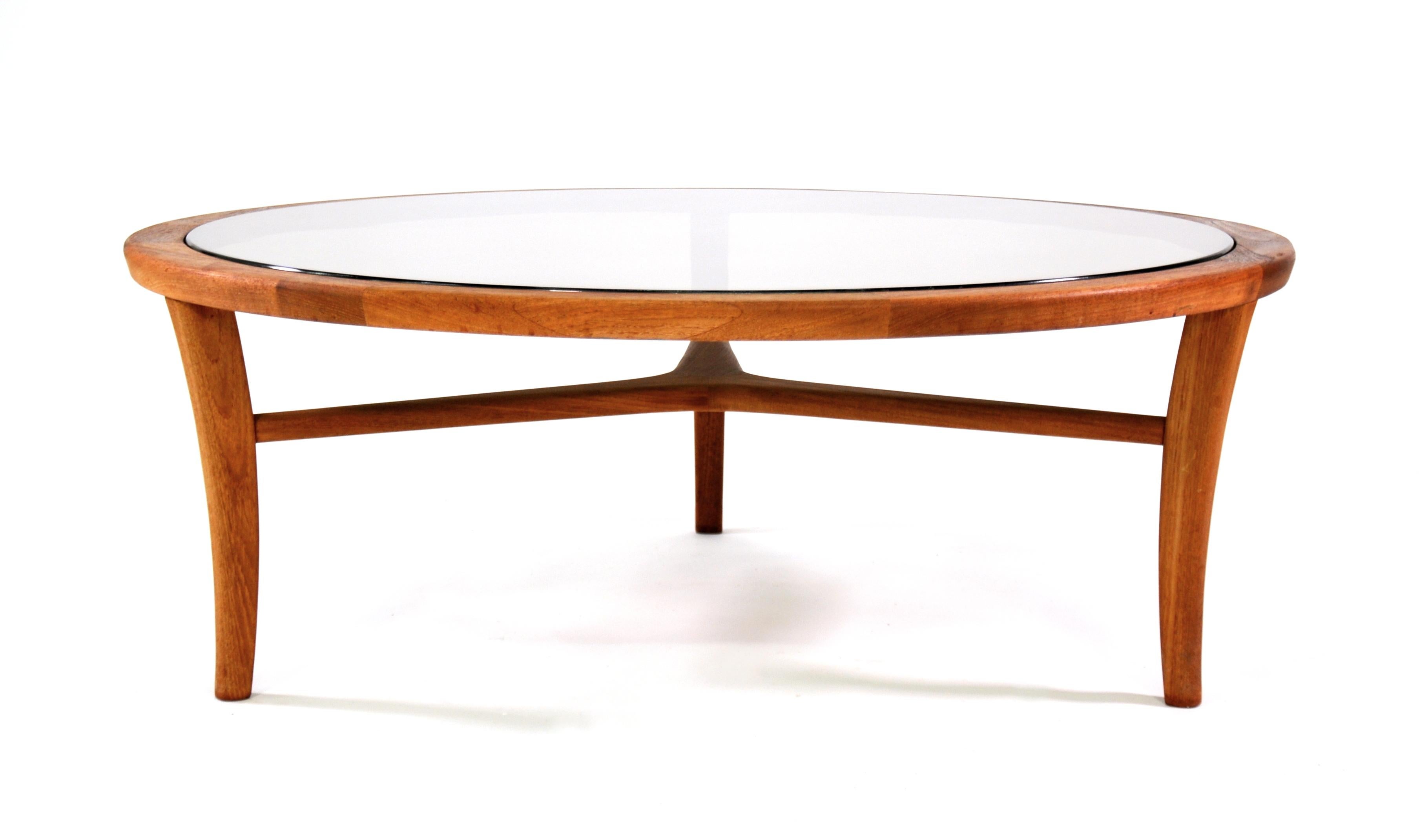 A vintage round cocktail table featuring a solid teak frame with an inset smoked glass top, dating from the 1970s. A pretty Scandinavian design that works well with Mid-Century Modern, eclectic or traditional interiors.