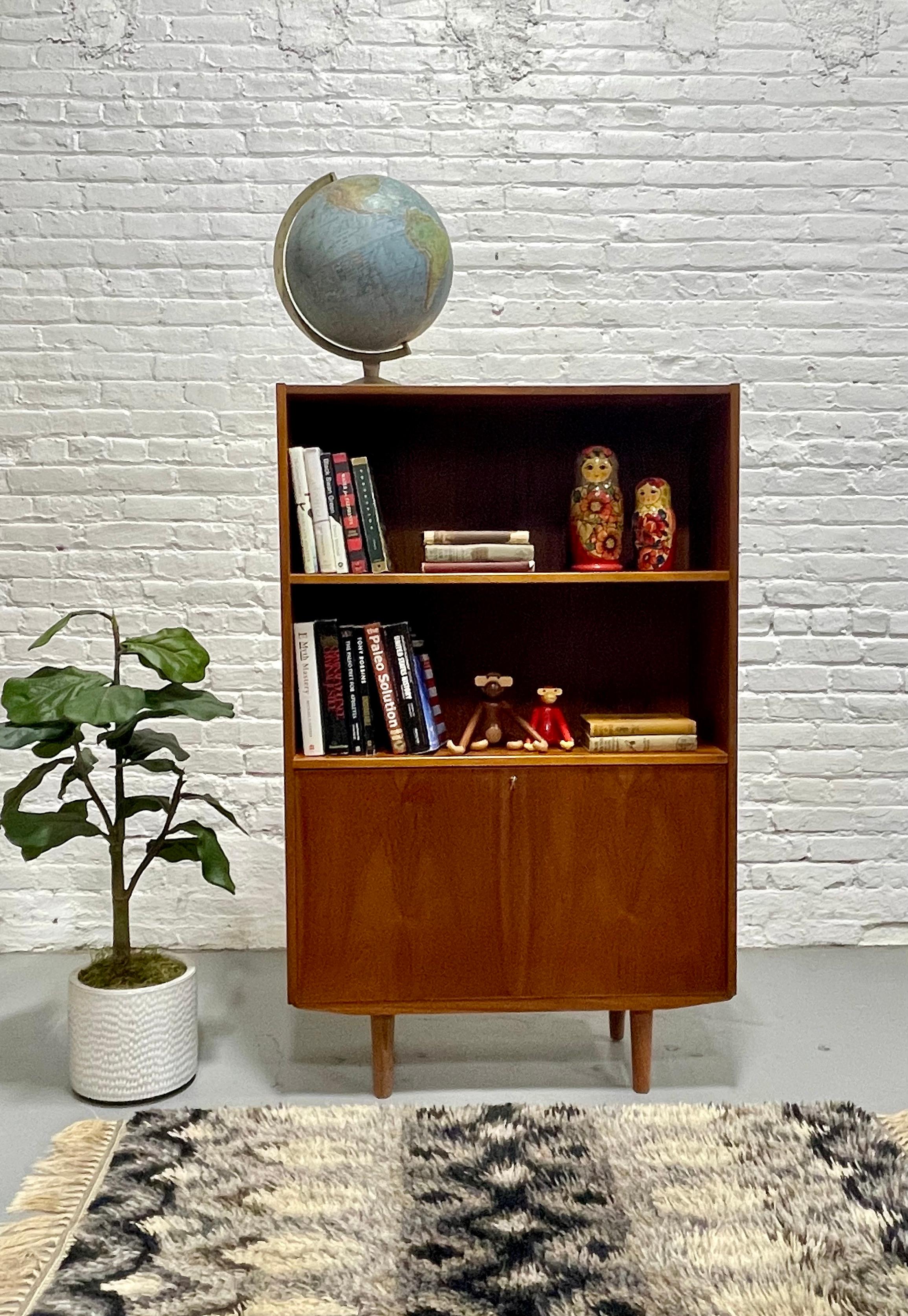 Danish Mid Century Modern Teak Bookcase / Liquor Bar Cabinet, c. 1960’s.  Loads of storage for all your books and collectables across the top two spacious shelving areas and a lockable (key included!) lower area for additional storage or as a mini