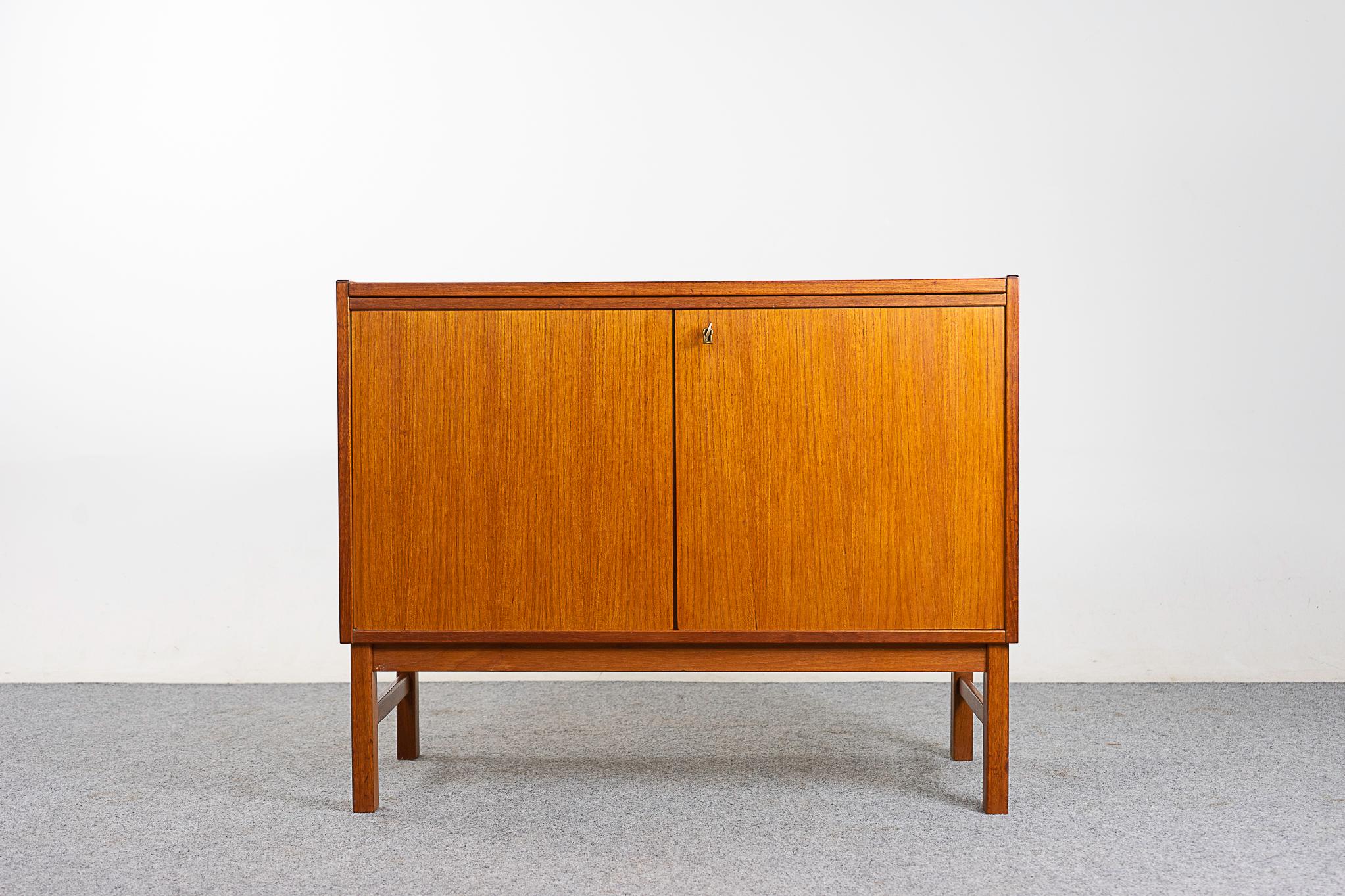 Teak midcentury cabinet, circa 1960s. Sleek, clean, simple lined design highlights the exceptional book-matched veneer throughout. Locking low profile cabinet with adjustable shelf, a perfect condo sized storage solution.

Unrestored item, some