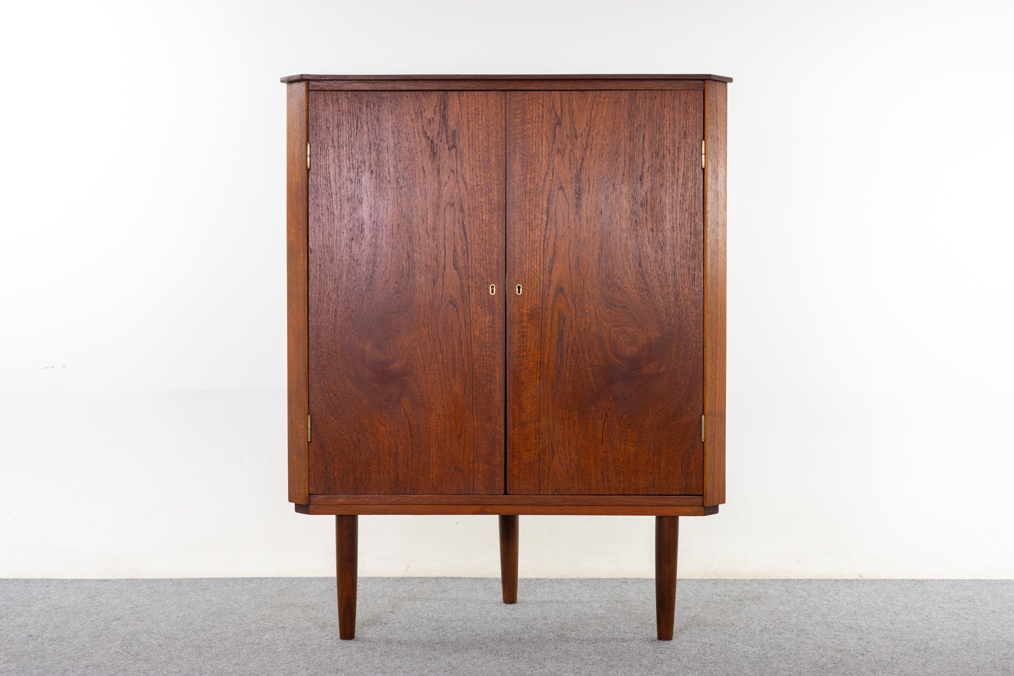 Mobile angolare danese in teak, anni '60 circa. Impiallacciatura in tinta con il libro, eleganti gambe affusolate e un ripiano regolabile. Doppie porte con chiusura a chiave e pannello posteriore appesantito per evitare che si rovesci. 