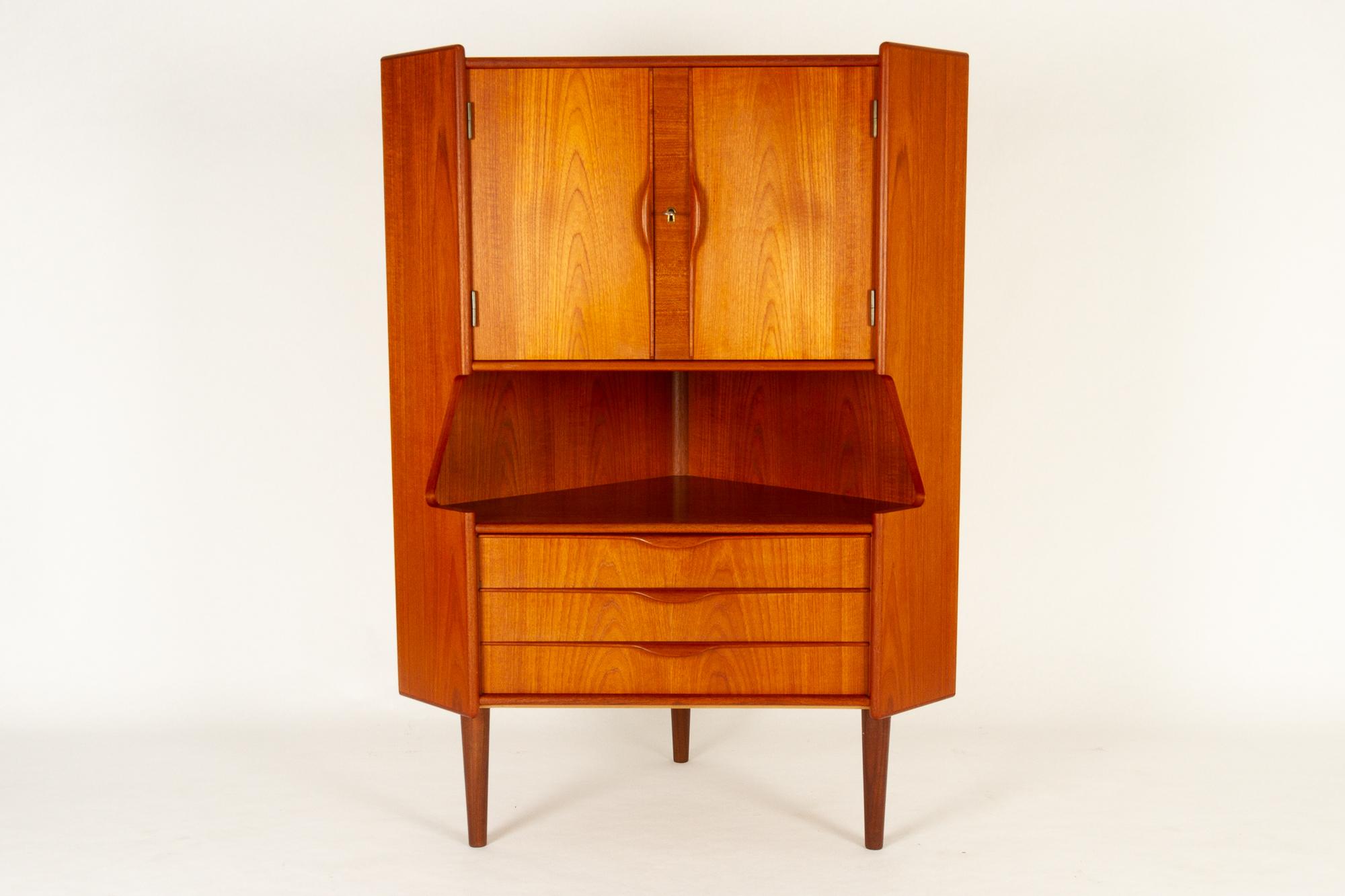 Danish Mid-Century Modern teak corner cabinet with bar unit, 1960s.
Very elegant cabinet with large mirrored bar unit, three wide drawers open shelf. Sculpted grips in solid teak. Double cabinet doors with lock and key. Bar unit has a black curved