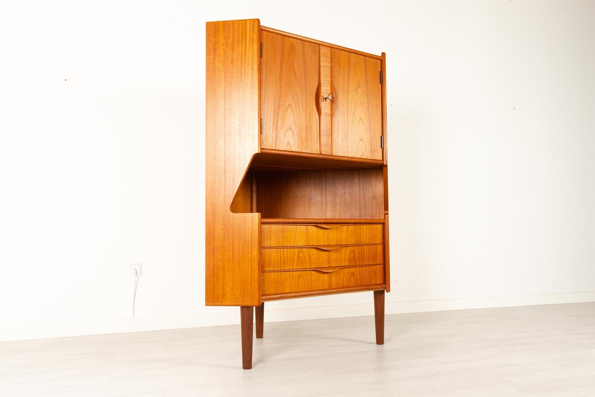 Danish Mid-Century Modern teak corner cabinet with bar unit, 1960s.
Very elegant cabinet with large mirrored dry bar, three wide drawers with dovetail joints and an open shelf. Sculpted grips in solid teak. Double cabinet doors with lock and key.