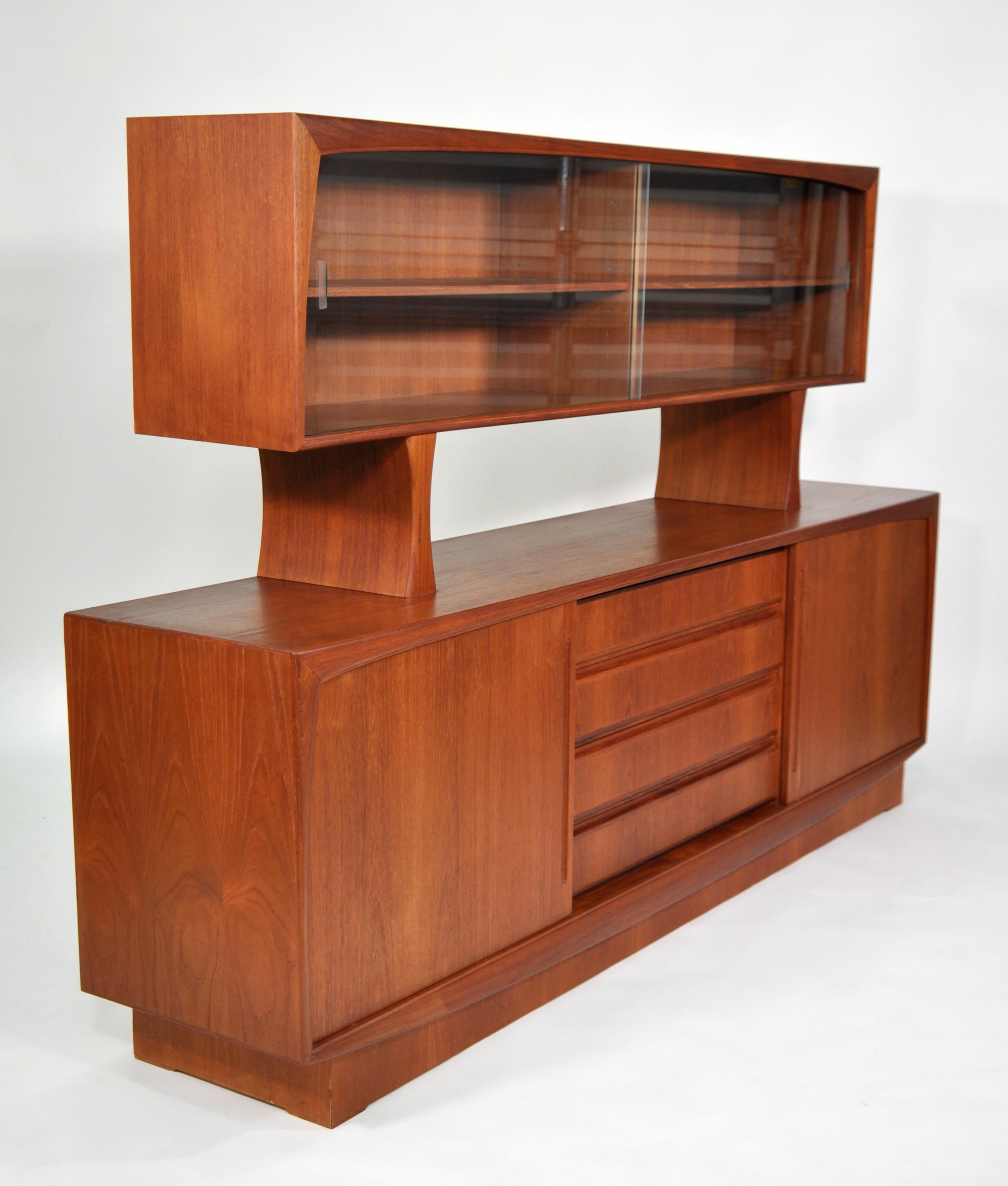 Beautiful vintage Scandinavian teak bar cabinet dating from the 1970s. The two-piece sideboard features two sliding doors opening to an interior fitted with a shelf, centering four drawers, on a plinth base. The removable display cabinet features a