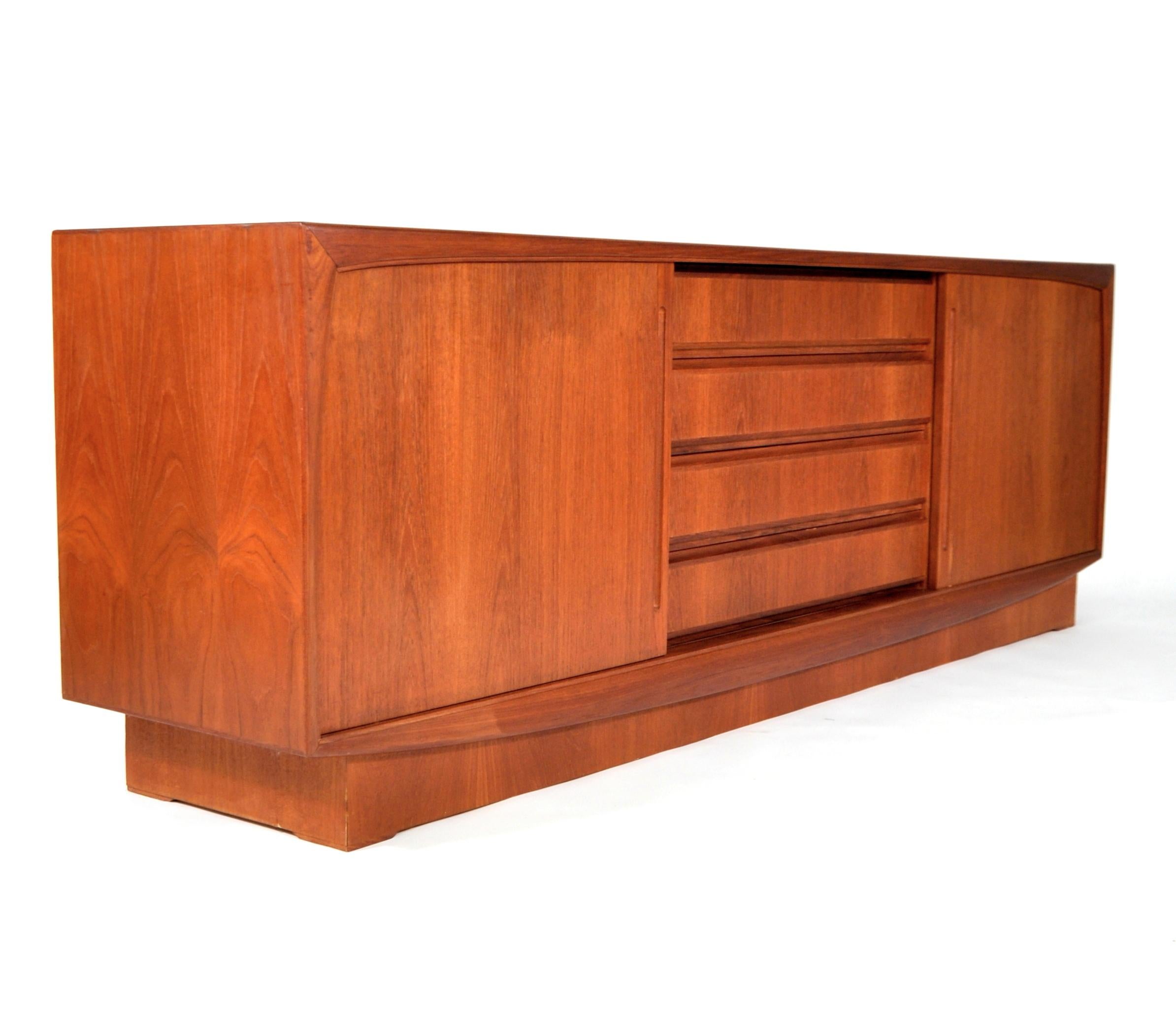 Beautiful vintage Scandinavian teak bar cabinet dating from the 1970s. The sideboard features two sliding doors opening to an interior fitted with a shelf, centering four drawers, on a plinth base. A versatile piece with simple and clean lines that