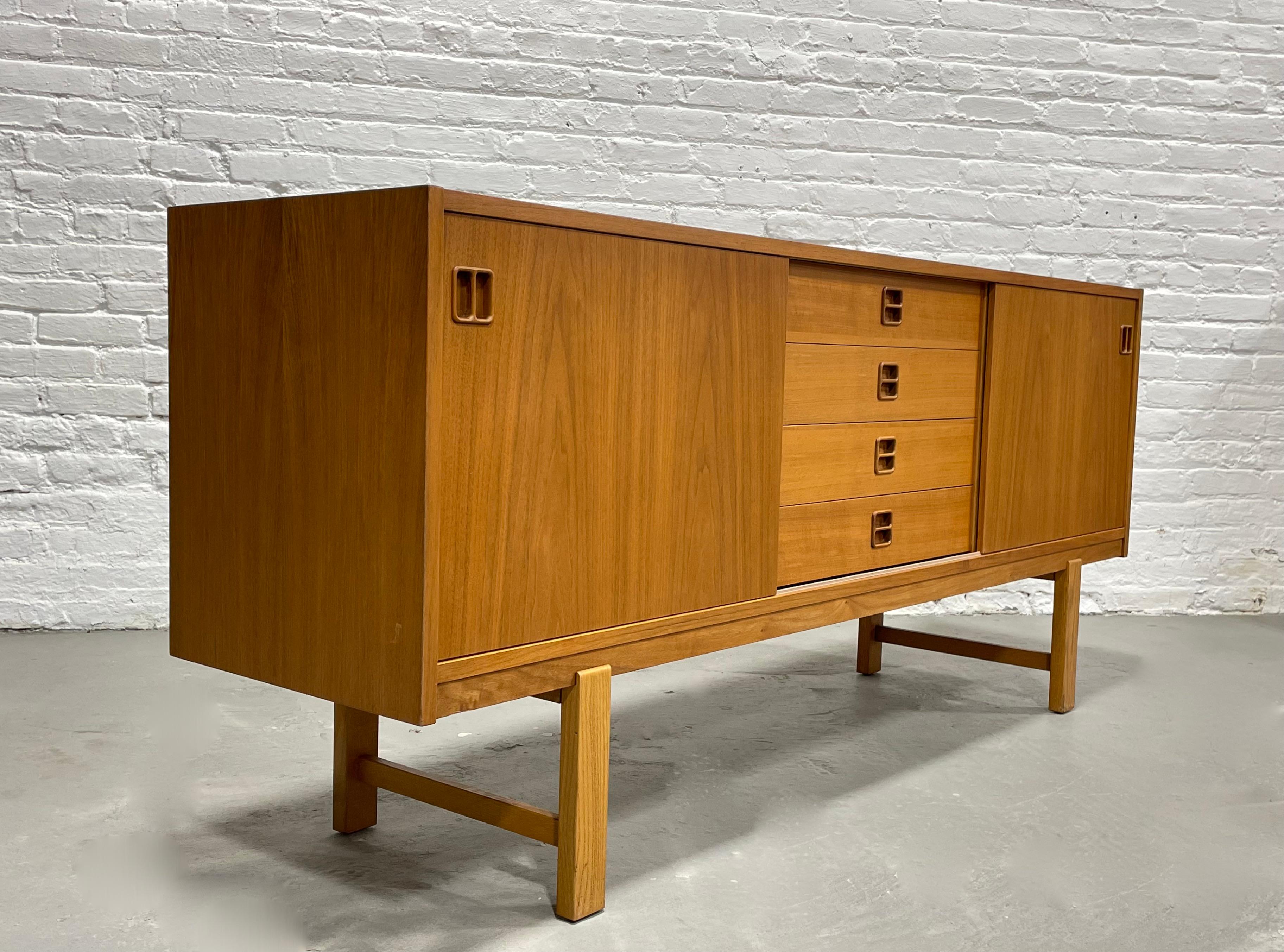 Mid-Century Modern Teak Danish sideboard, circa 1960s. Two sliding doors with a generous shelving area along each side and 4 dovetailed drawers along the center with unique hand-pulls. The top drawer features a green felt lined silverware drawer.