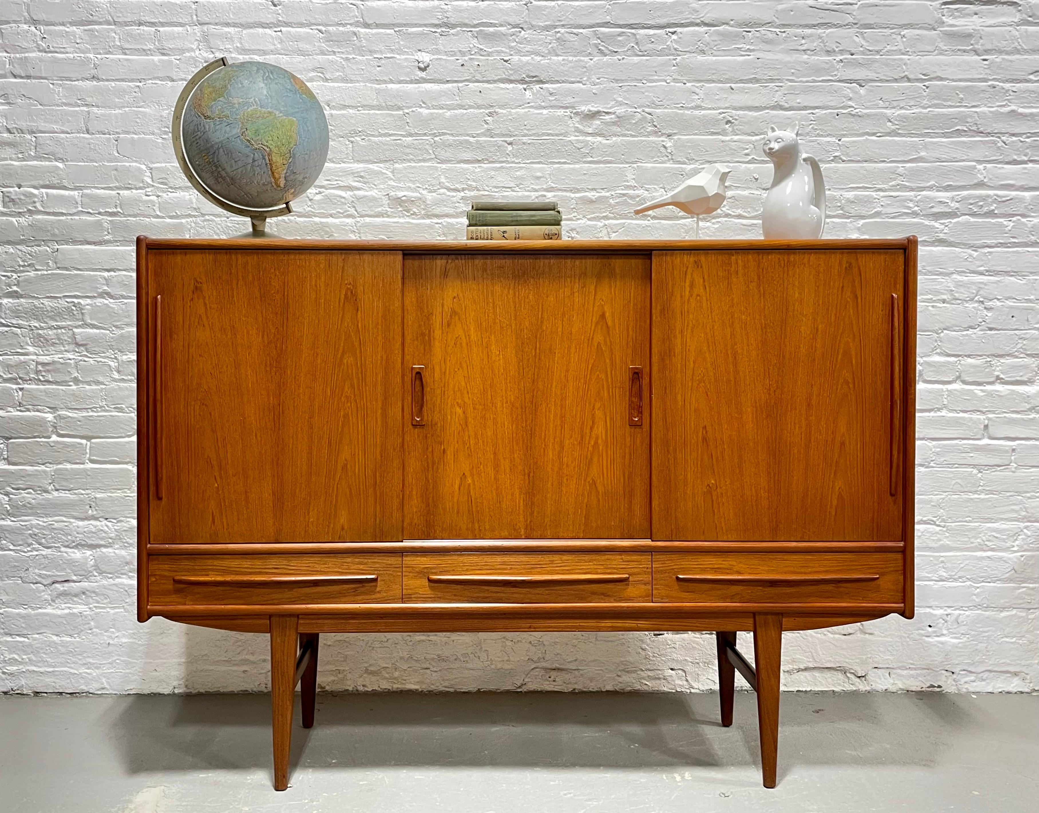 Stunning Mid Century Modern Danish Teak Highboard Credenza / Sideboard, c. 1960's. This incredible piece is gorgeous in its simple yet extremely functional design. This beauty offers  three sliding door compartments with loads of shelving storage