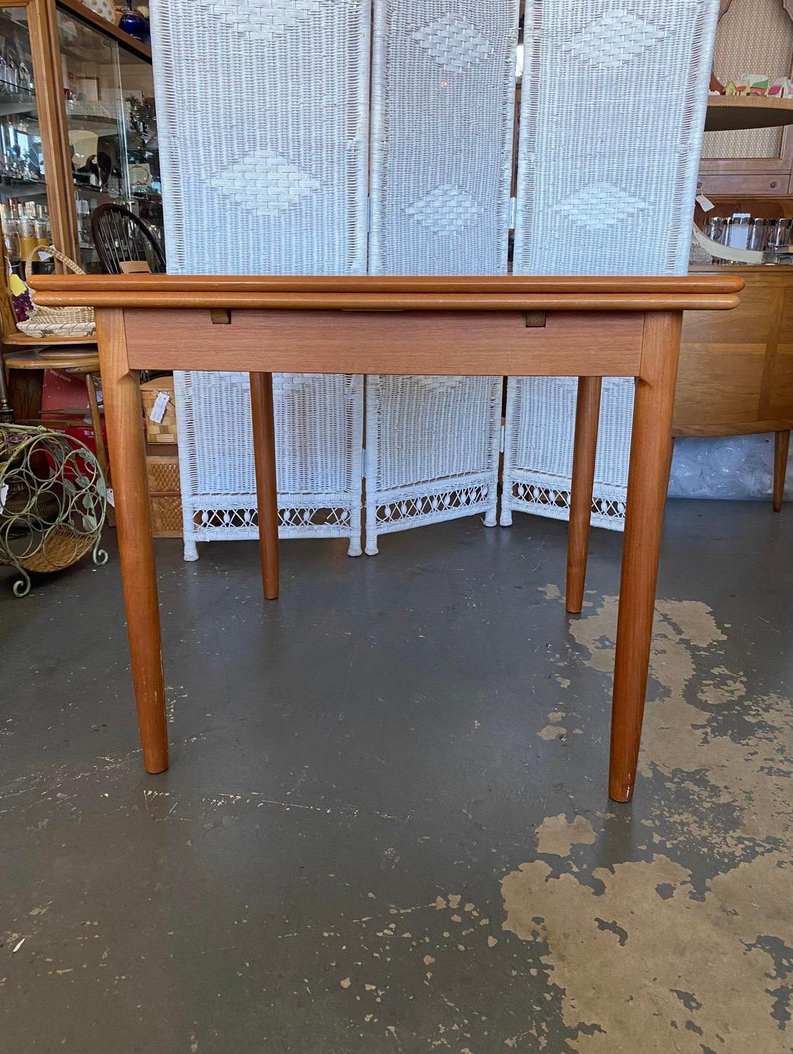 Great Mid-Century Modern teak, square dining table made by AM (Ansager Mobler) in Denmark. This table is an excellent space saver that can easily turned into a full dining table seating 6 when extended using both pullout leaves. Fully extended, the