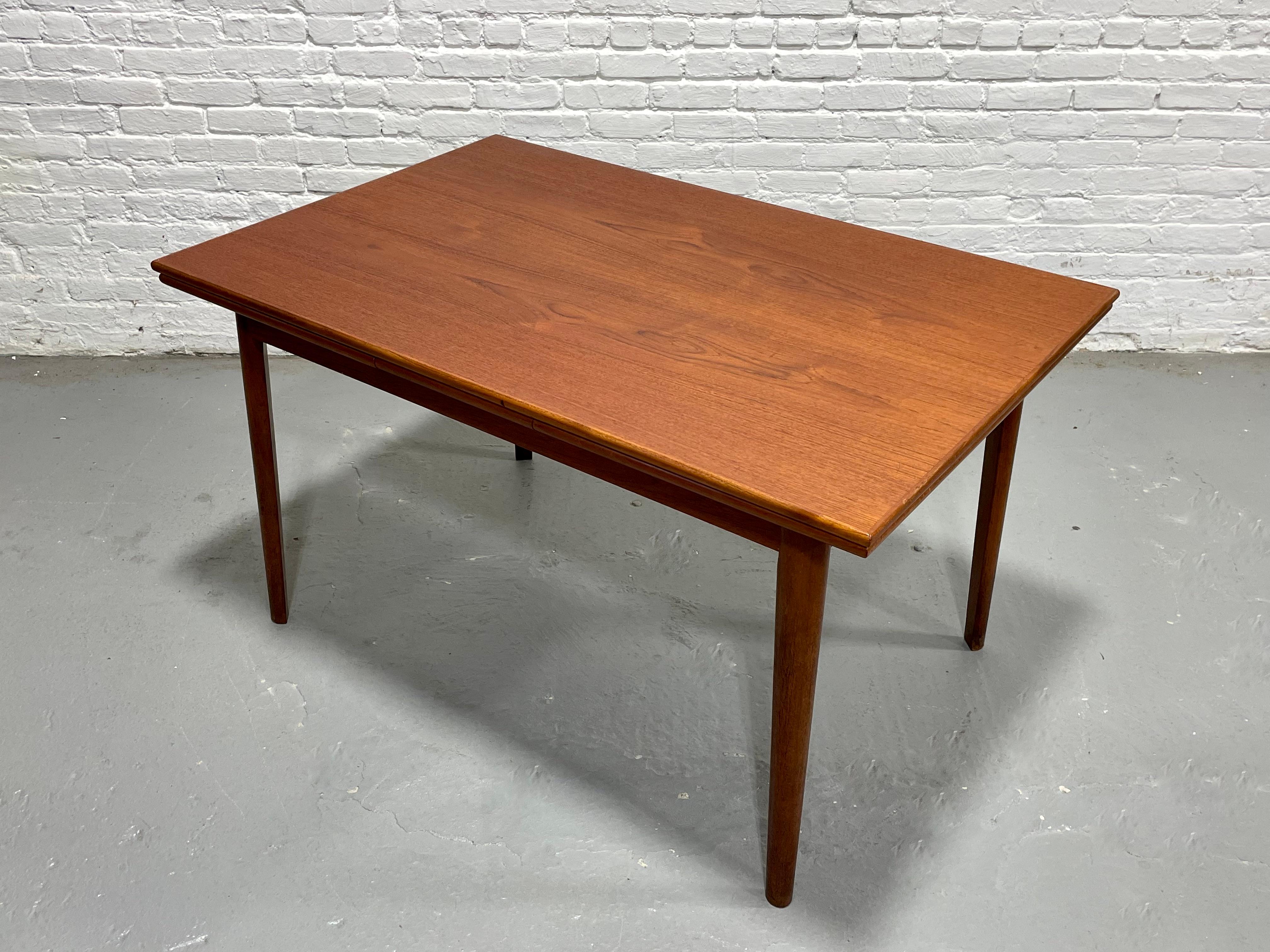Danish Mid Century Modern TEAK DINING TABLE with two hidden leaves in a lovely streamlined size, perfect for smaller homes. The table is impeccably crafted with stunning wood grains and features two hidden leaves underneath the tabletop that easily
