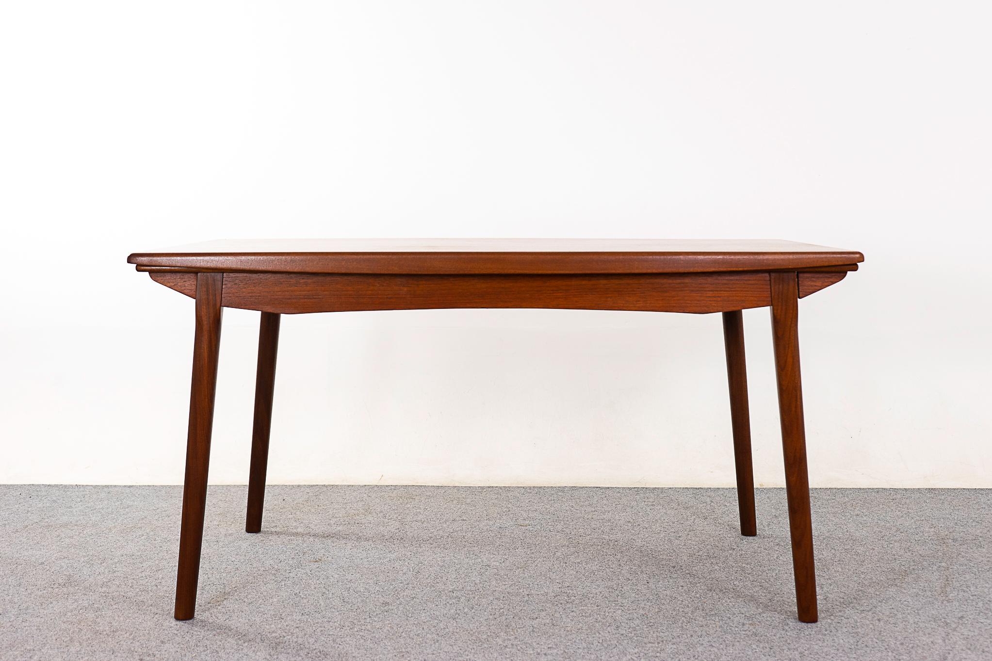 Teak mid-century dining table, circa 1960's. Splayed legs and unique arching apron. Top is framed with solid wood edging, veneered top with book-matched grain. Self-storing leaves slide out from each end to extend the table surface by nearly two