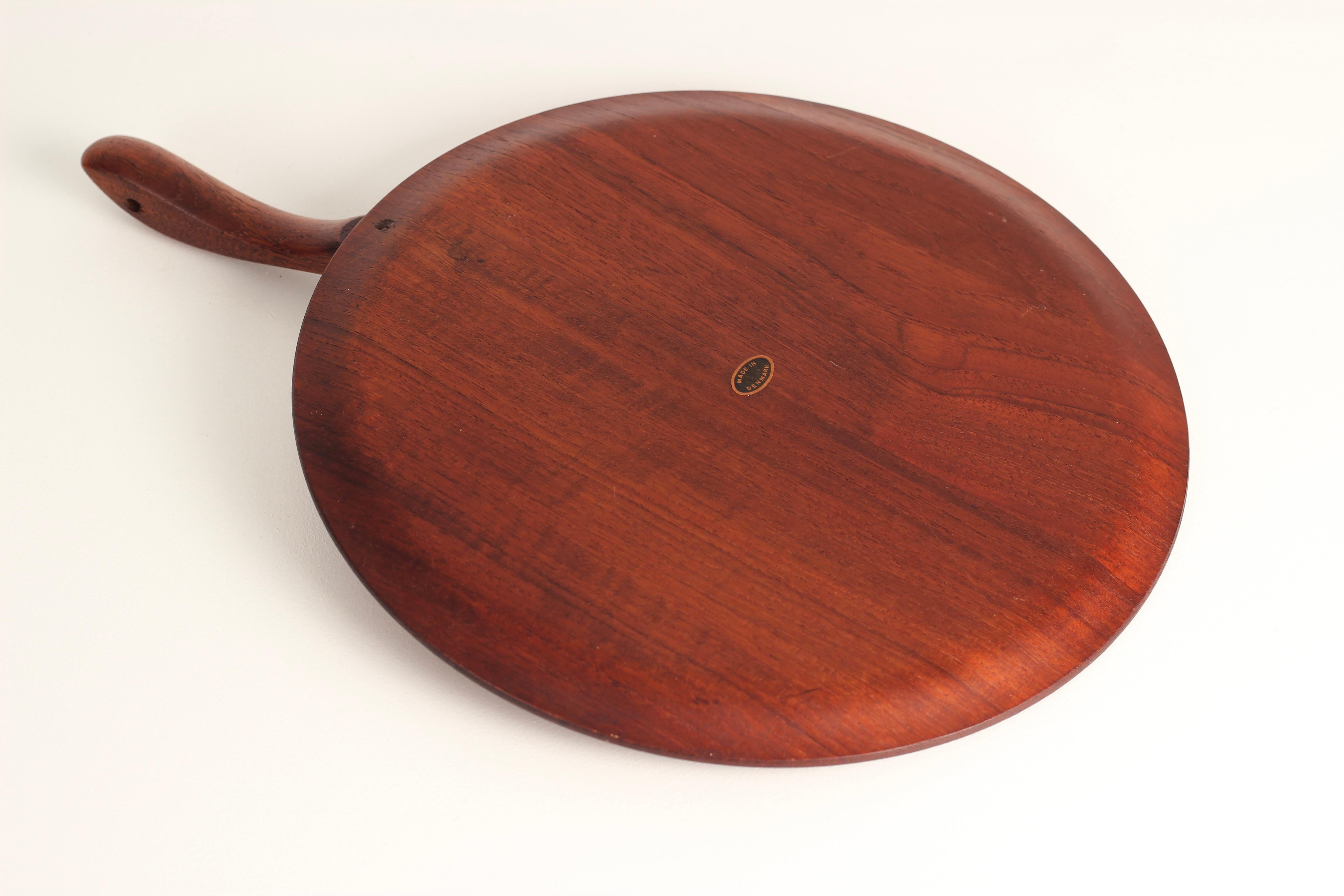 A Danish Mid-Century Modern Scandinavian design serving platter or cheese board in the style of Kay Bojesen. A sleekly designed handle with a hole for a strap to hang, glides over the top of a steam bent circular plate with angled profiled edges.