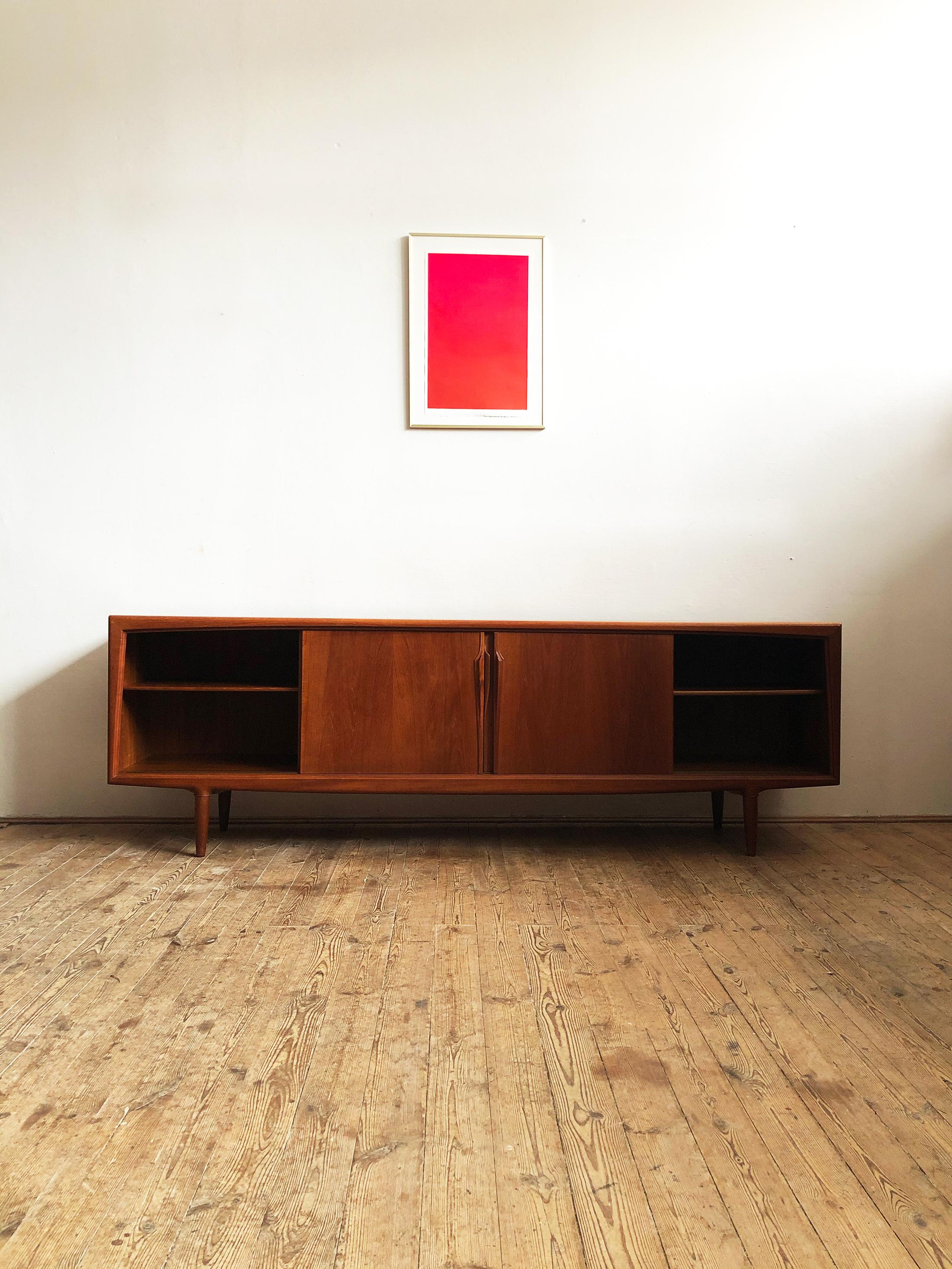This Mid-Century Modern teak sideboard was designed in the 1950s for Axel Christensen Odder Møbelfabrik in Denmark. 

It shows exquisite Danish craftsmanship and offers plenty of storage space on four tapered legs and lots of beautiful details
