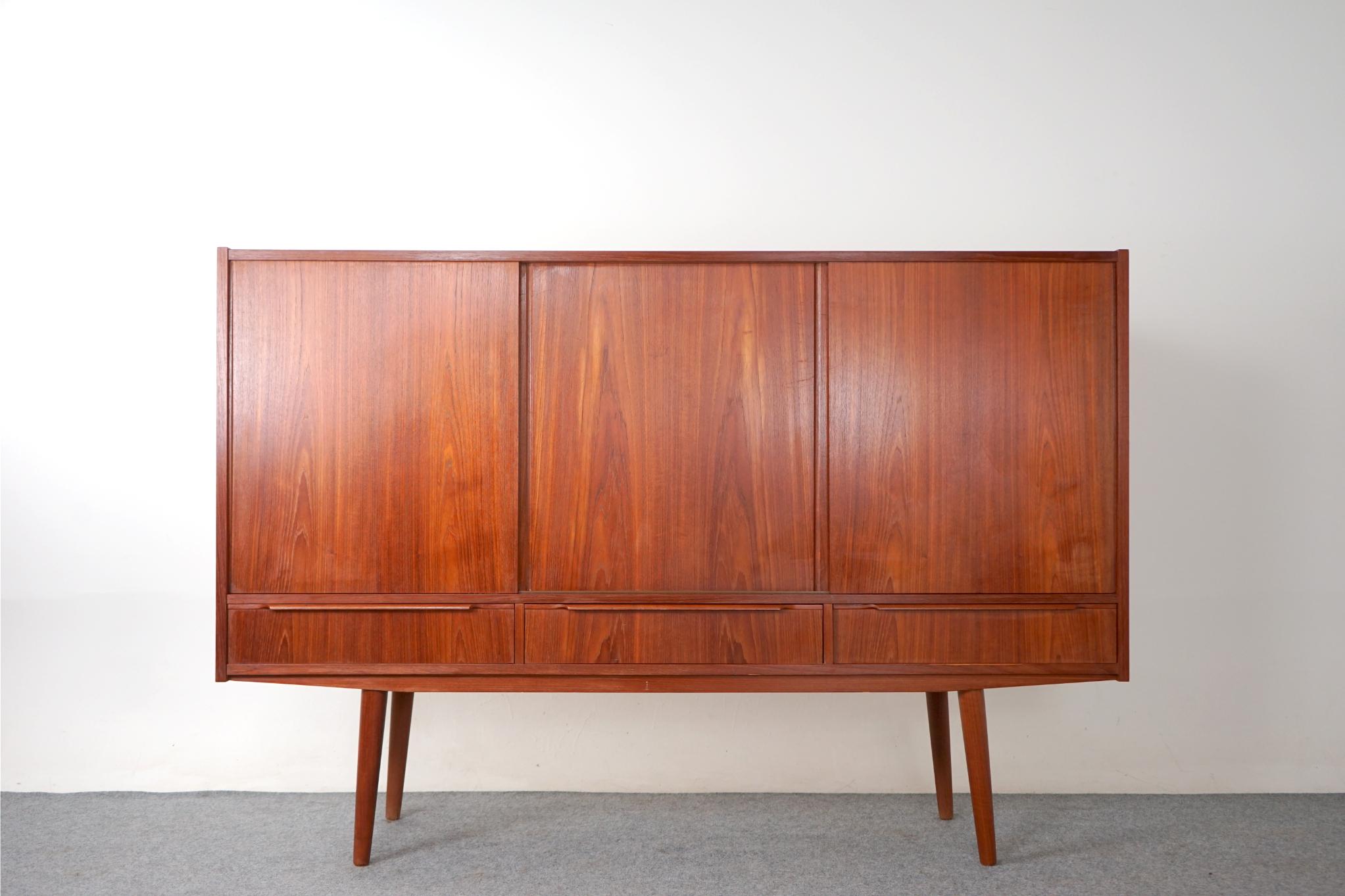 Teak Danish sideboard, circa 1960's. Clean, simple lined design with exceptional book-matched veneer. Sliding doors and exterior drawers offers ample storage. Interior bays are outfitted with removable shelving, side section offers a mirrored bar