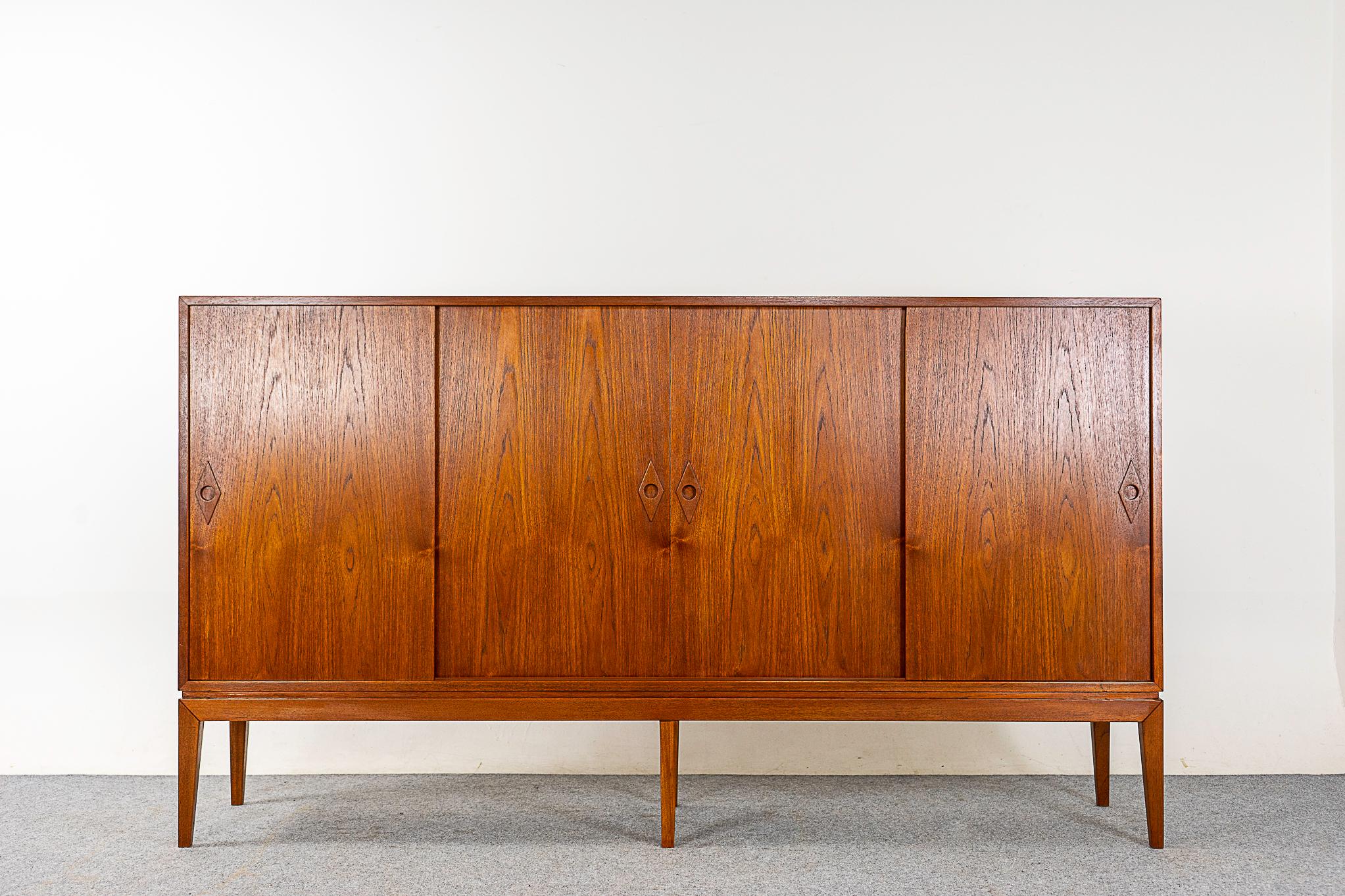 Teak Danish sideboard, circa 1960s. Generously proportioned design with warm toned book-matched veneer throughout. Darling diamond shaped finger pulls on the sliding doors. 6 adjustable shelves and 6 drawers with lovely corner joinery. Find all of