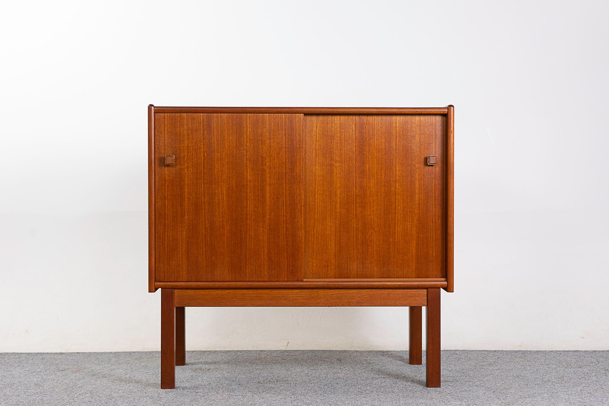 Teak Danish modern cabinet, circa 1960s. Low profile sliding door cabinet with interior shelf and darling pulls. Clean, simple lined design with lovely book-matched veneer. We have a matching pair, which would look 