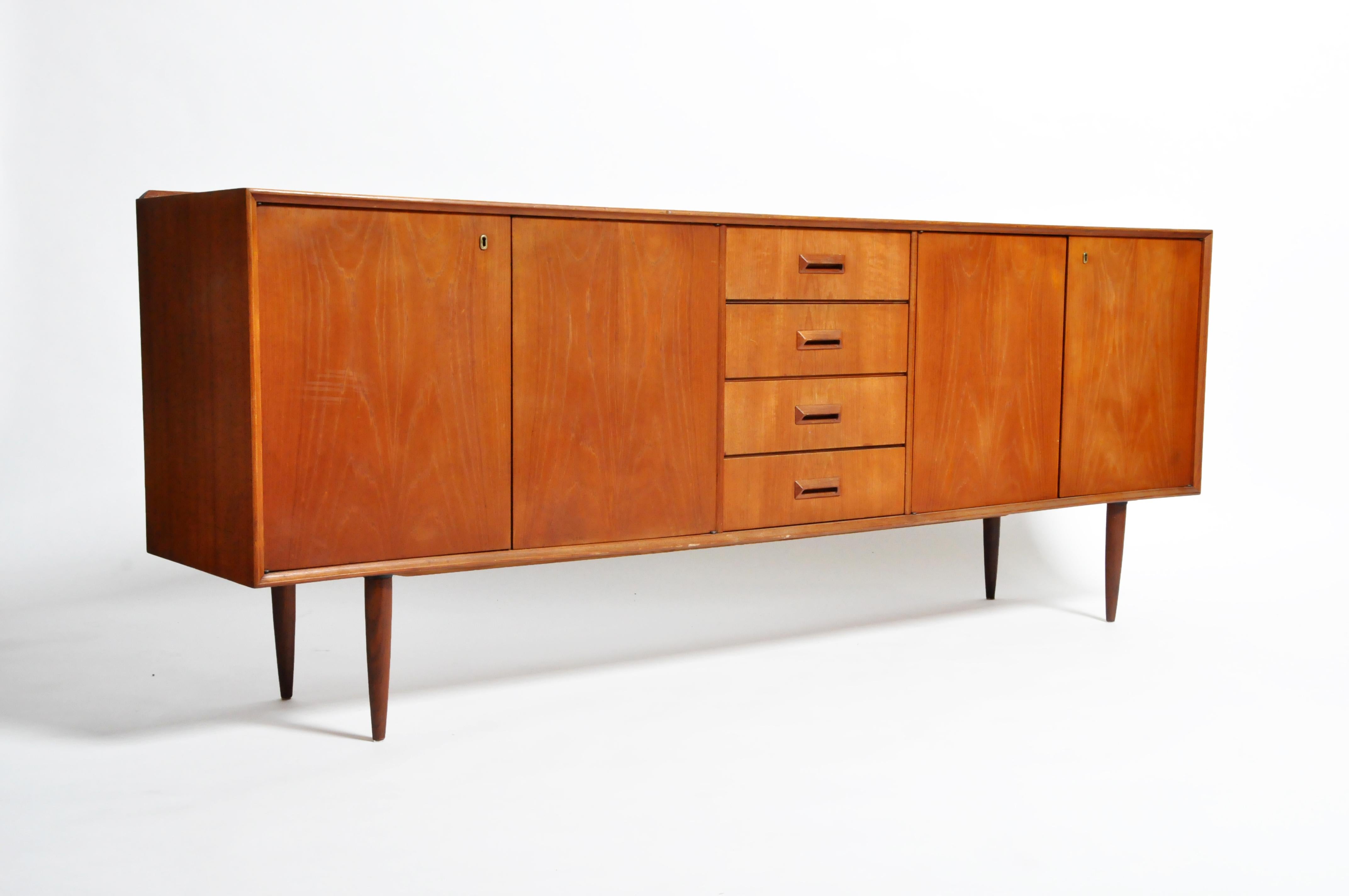 This handsome Mid-Century Modern sideboard is from Denmark and was made from teak wood veneer, circa 1960. This piece features four drawers and four doors that open up to shelves for storage.