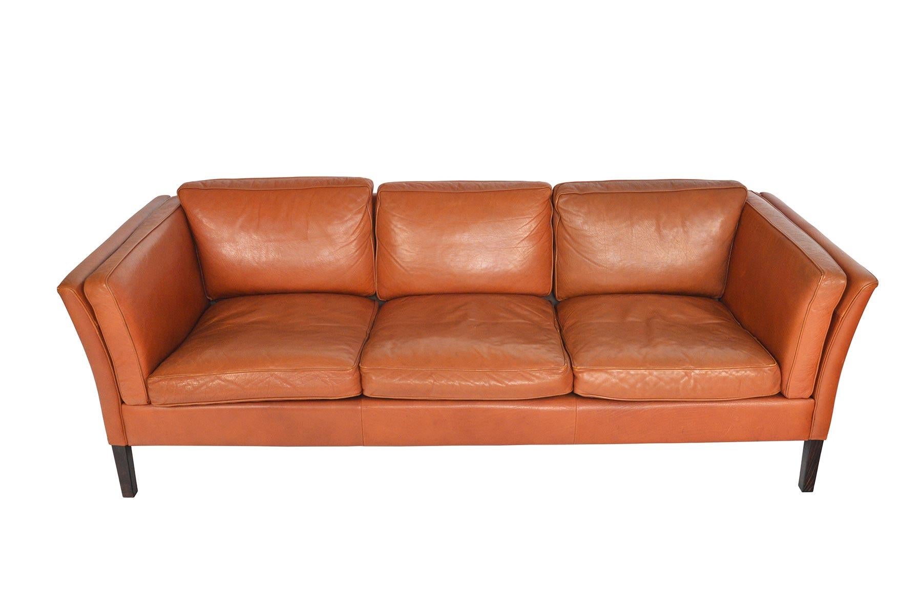This Danish modern three seat sofa is covered in original caramel colored leather. The gently bowed arms support two arm cushions. Six cushions nestle in the frame. Piece stands on stained oak legs. In excellent original condition.

 