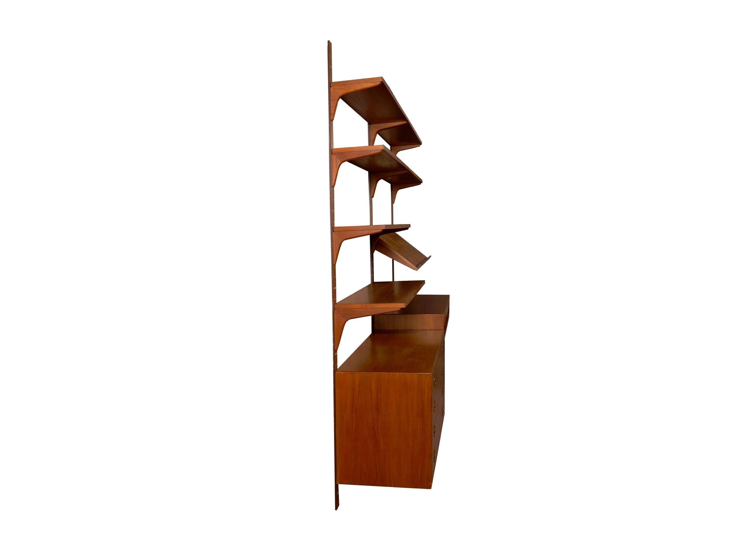 A sleek Mid-Century Modern teak modular wall unit with shelving over a chest of drawers on one side and a desk top on the other, it was designed by Rud Thygesen and Johnny Sorensen for HG Furniture in Denmark. The wall unit is entirely adjustable