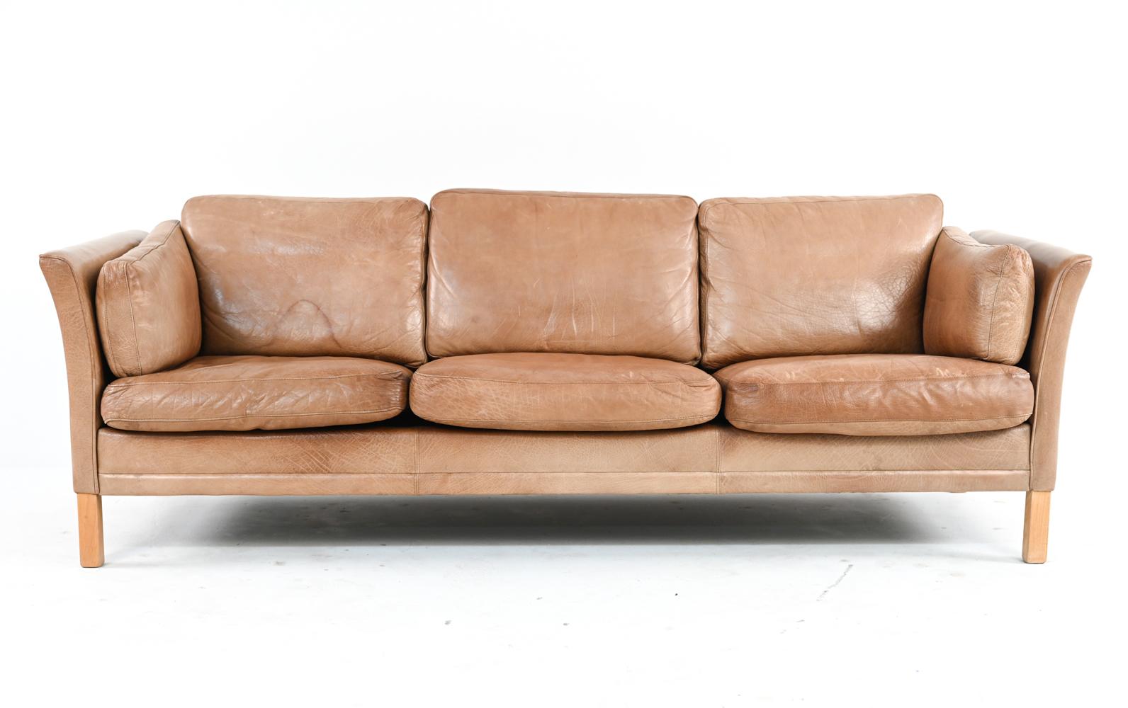 This classic three-seat sofa by Mogens Hansen is elevated by the addition of thick, luxurious buffalo leather upholstery, renowned for its durability and wide grain. In this example, the tan hide has produced a beautifully varied patina over time,